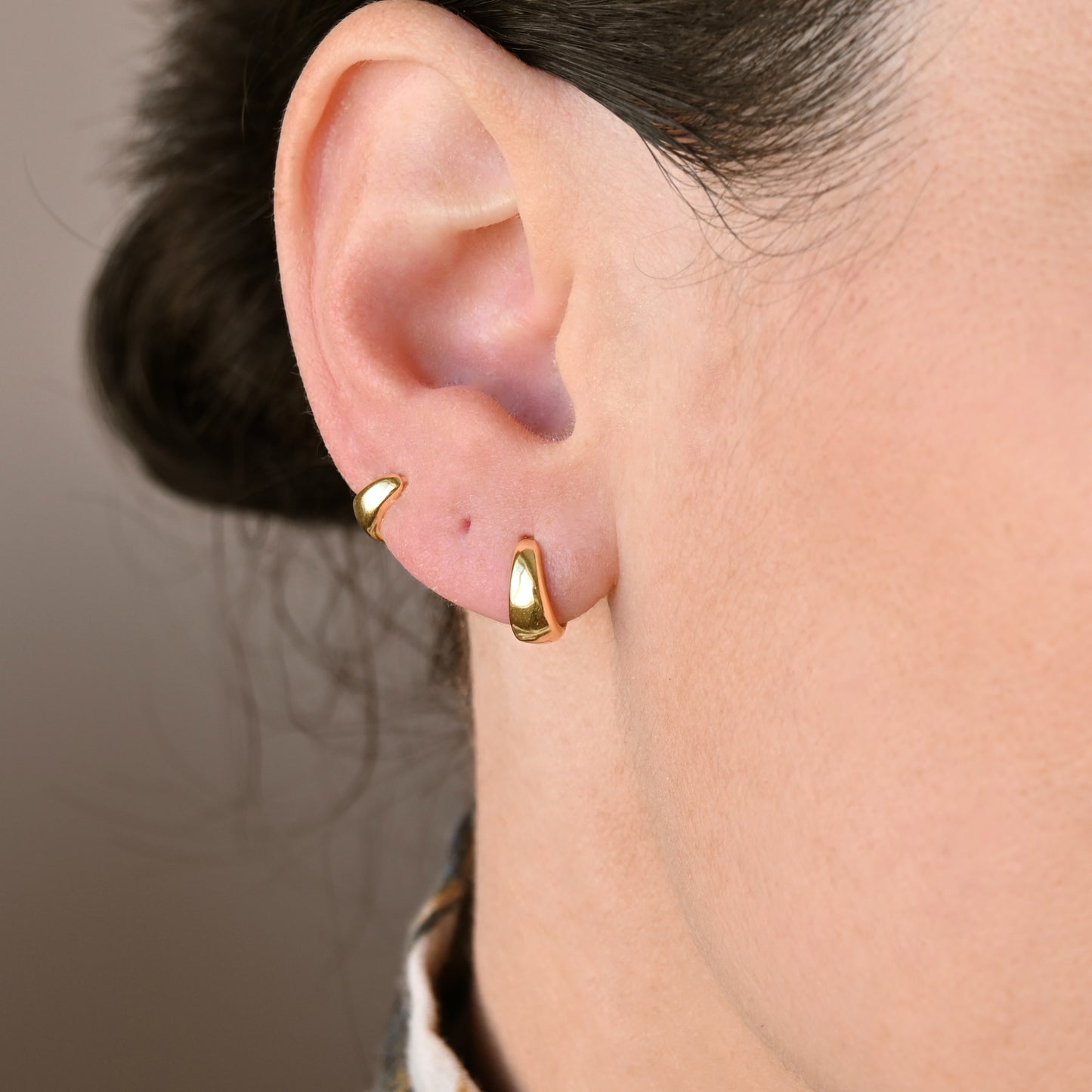 Two gold dome hoop earrings, 10mm and 8mm, worn by a person with a neutral background