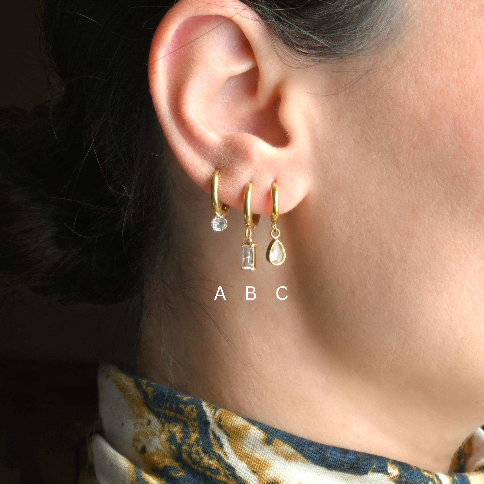Close-up of an ear wearing gold hoop earrings with small diamonds 