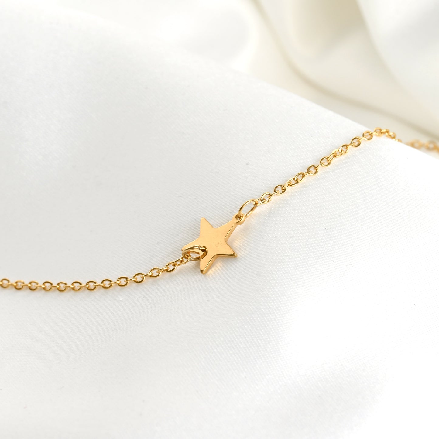 Gold necklace  with a star charm on a delicate cable chain against a white background
