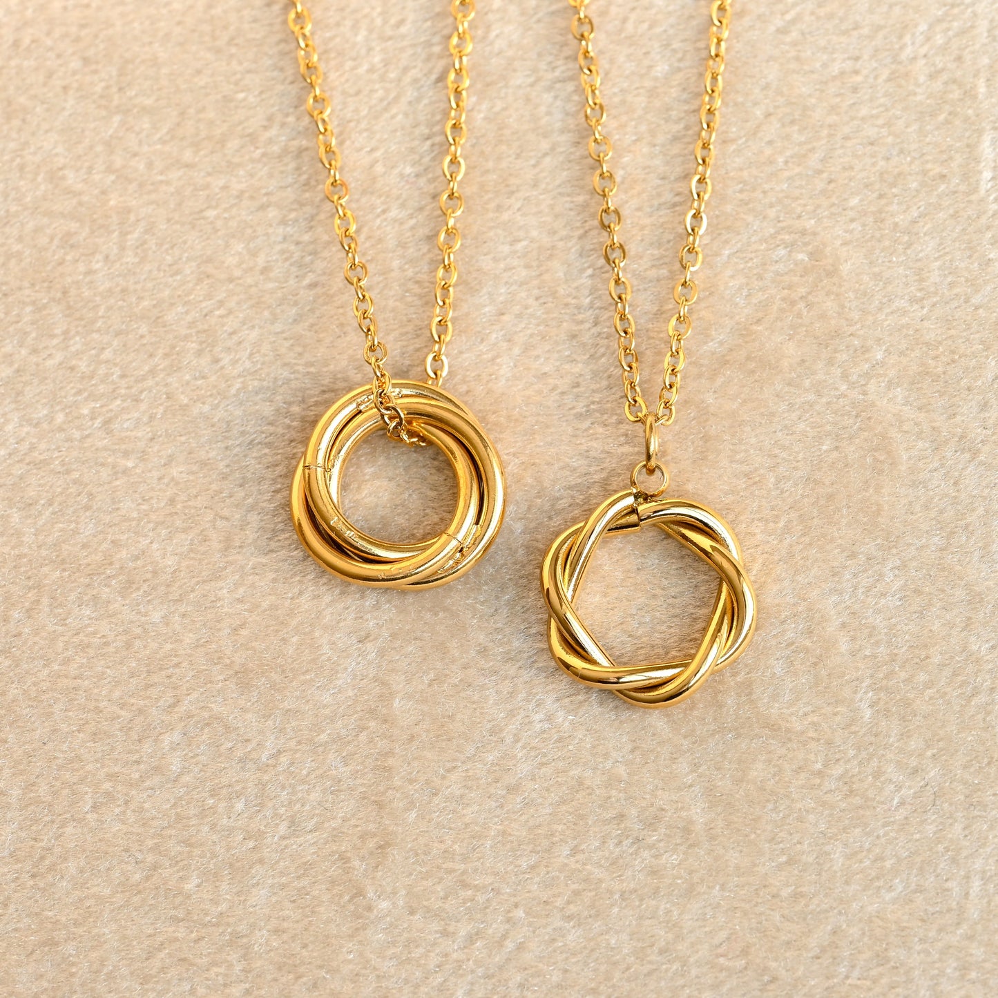 Two gold karma necklaces with interlocking ring pendants on a beige background