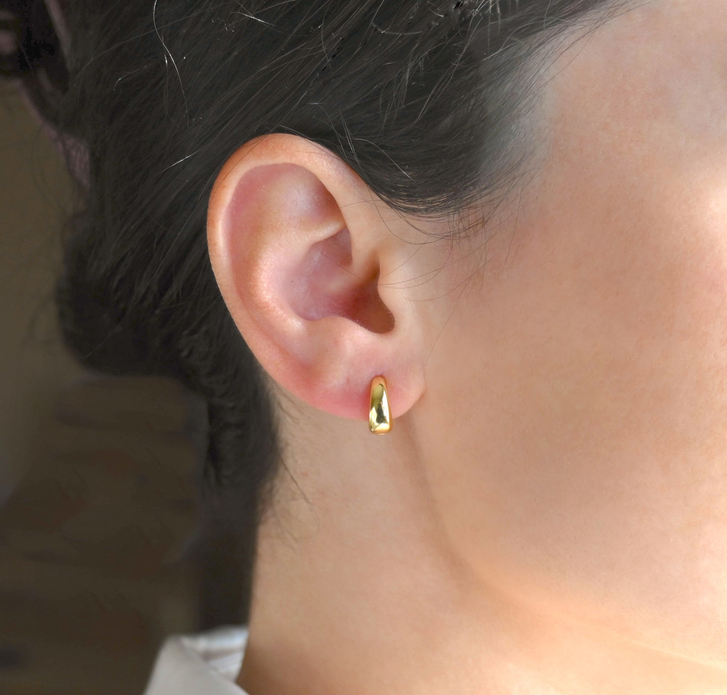 Close-up of a person wearing a thick gold hoop earring with a blurred background