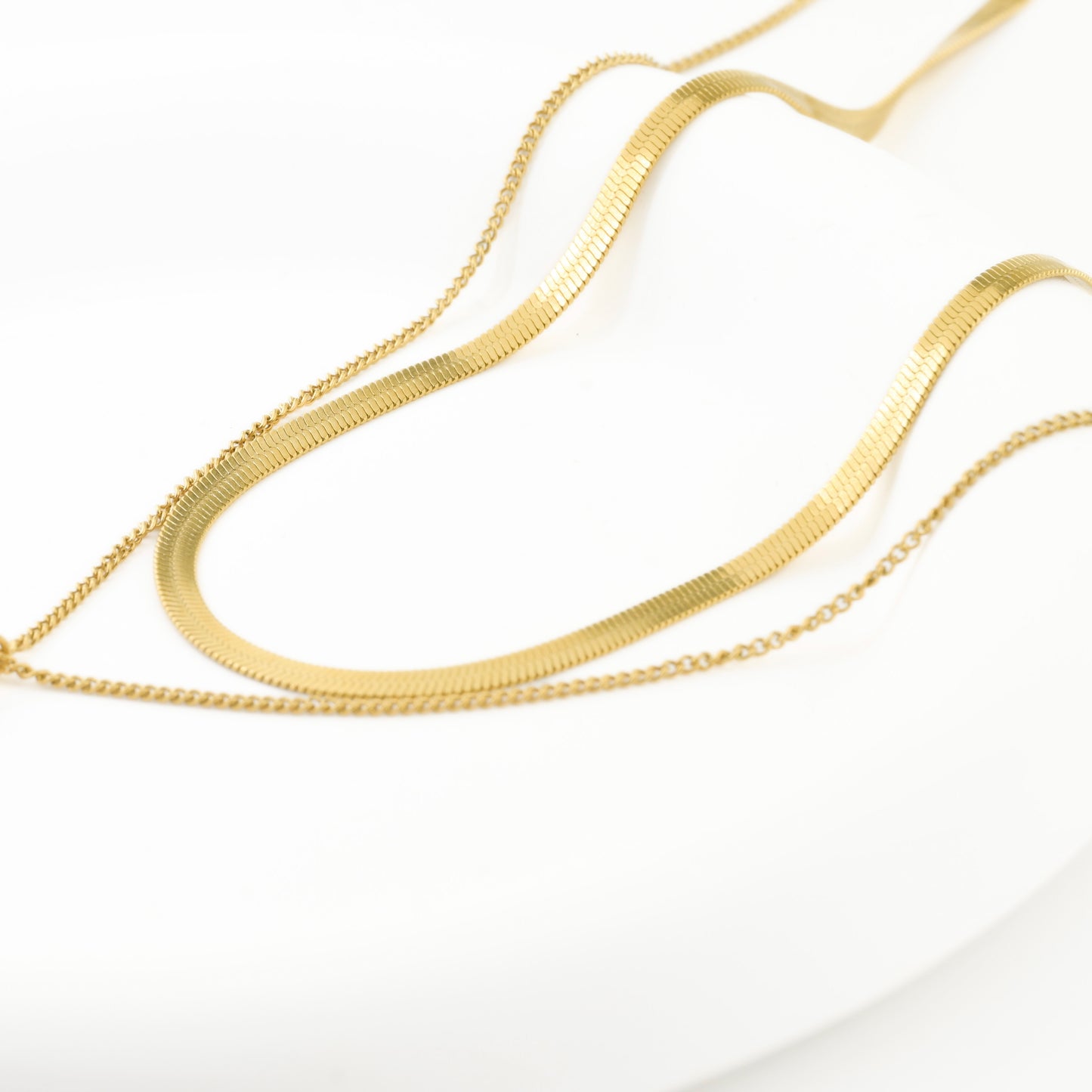 Close up view of gold  herringbone and curb chains on a white background
