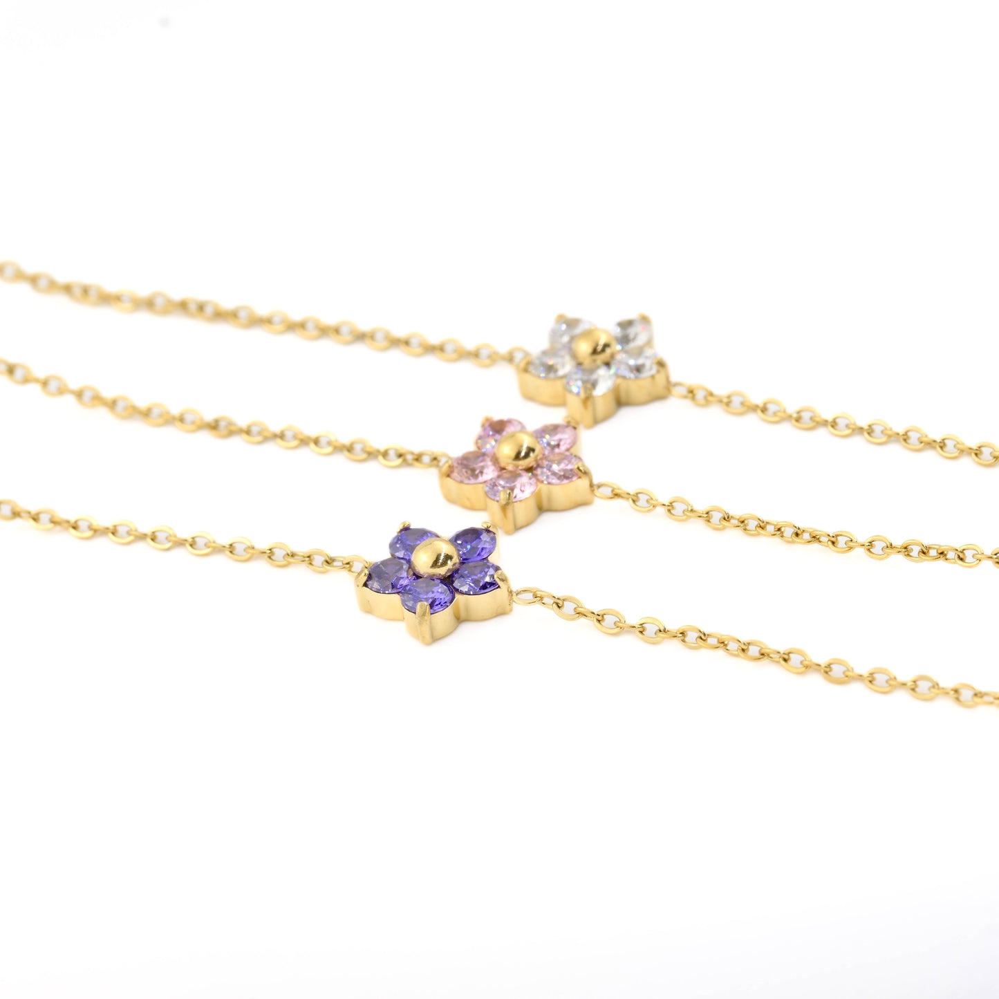 Three gold flower charm bracelets featuring purple, pink and clear gemstones on a white background.