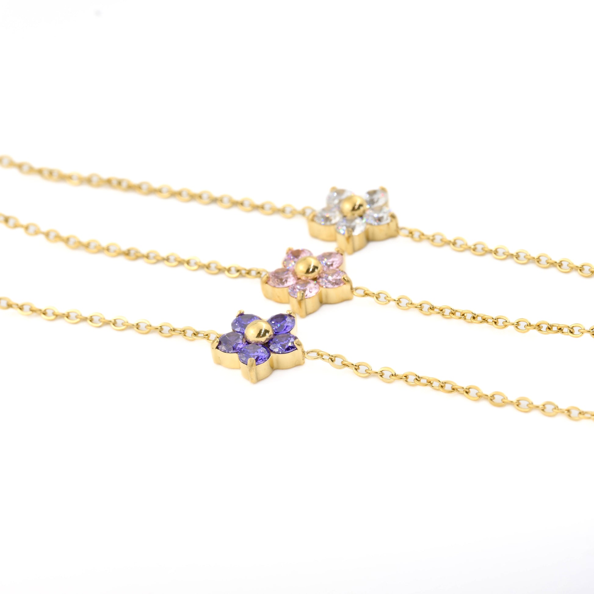 Three gold flower charm bracelets featuring purple, pink and clear gemstones on a white background.
