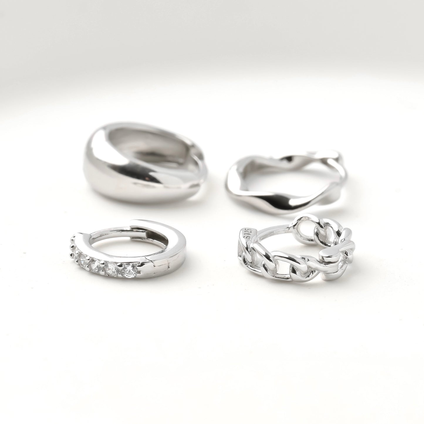 Set of small silver hoops including half eternity pave CZ, curb link chain, twisted and chunky dome on a white background