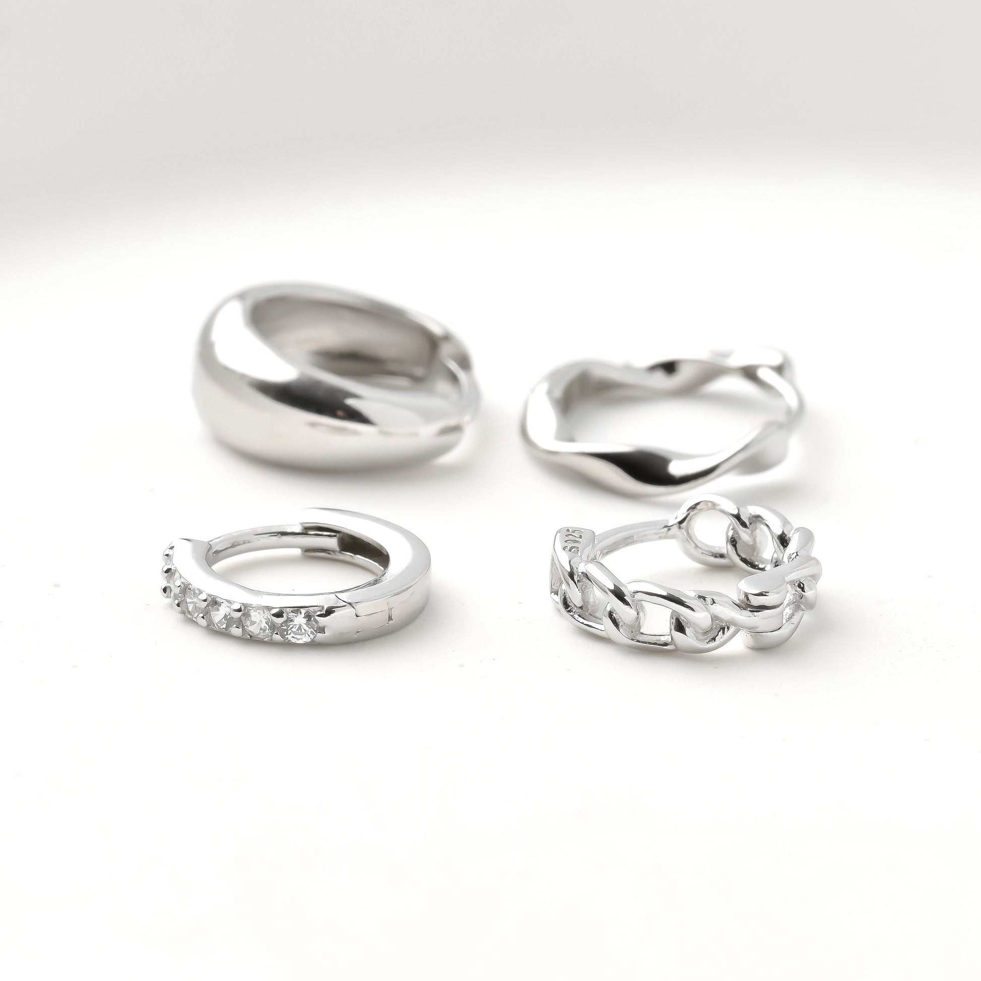 Set of small silver hoops including half eternity pave CZ, curb link chain, twisted and chunky dome on a white background