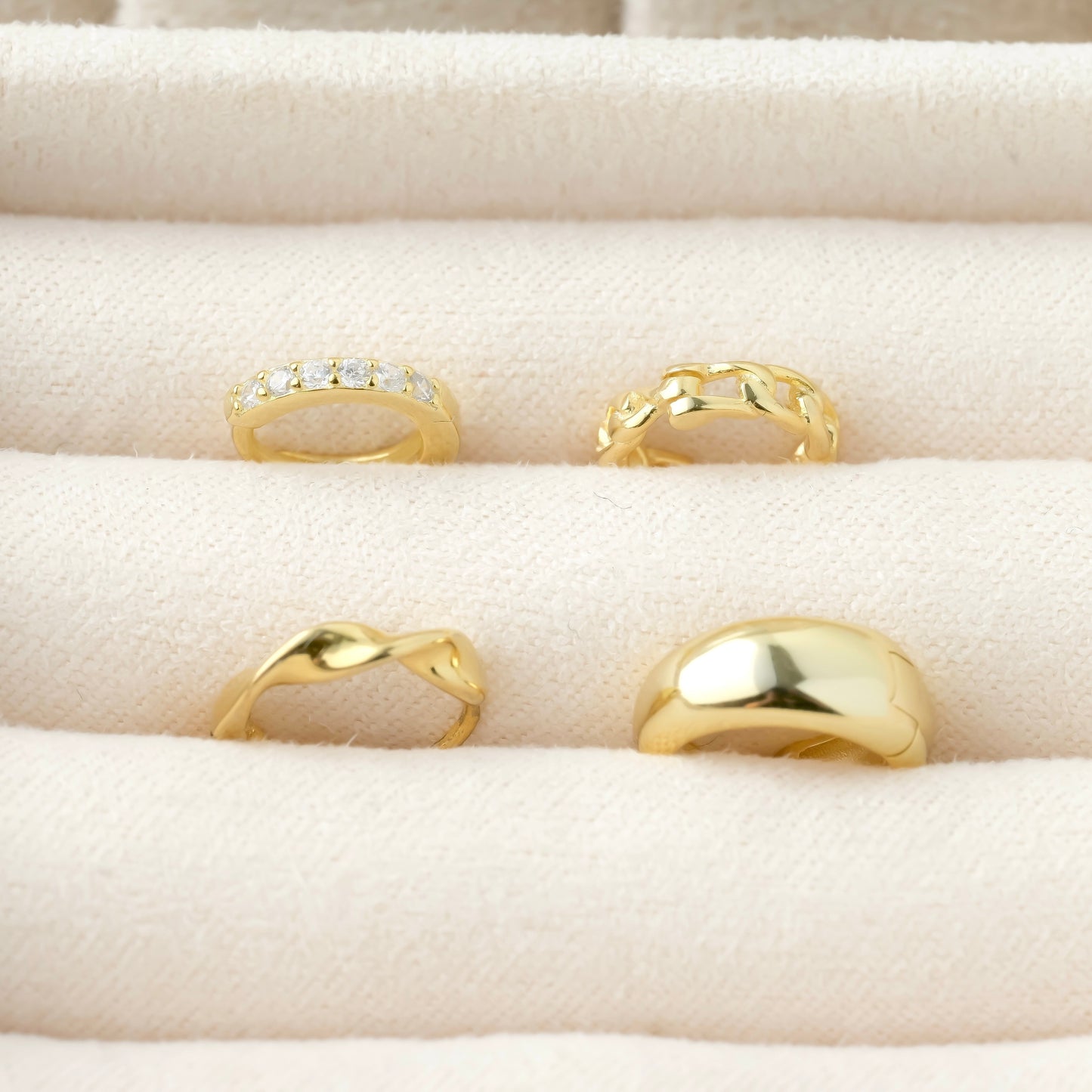Set of gold huggie earrings on a beige cushioned surface