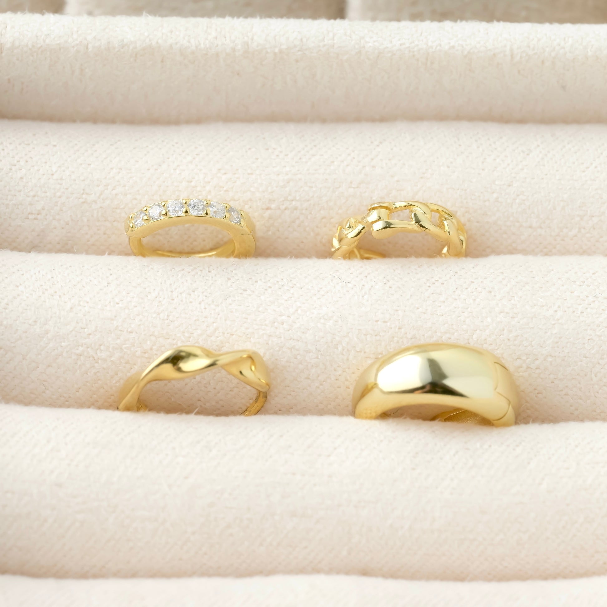 Set of gold huggie earrings on a beige cushioned surface