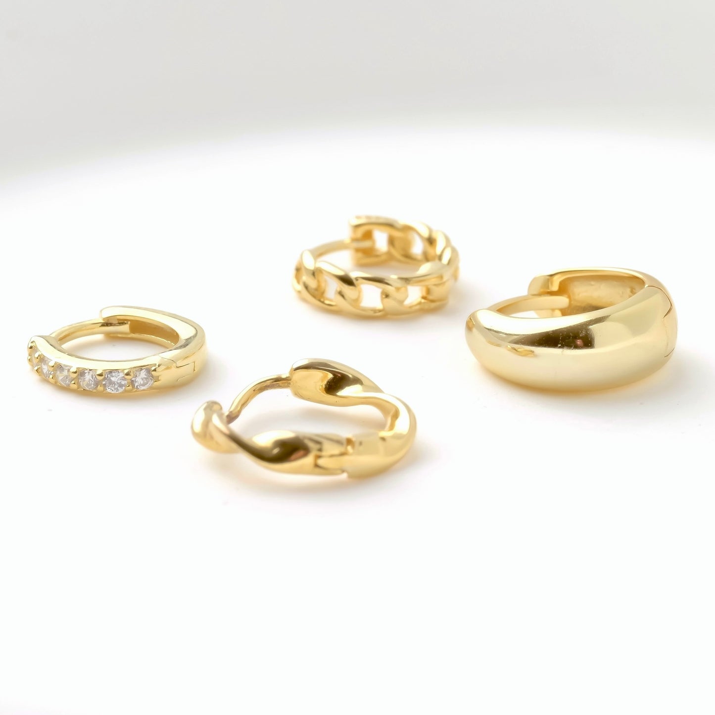 Set of mini gold hoop earrings including half eternity pave CZ, curb link chain, twisted and chunky dome on a white background