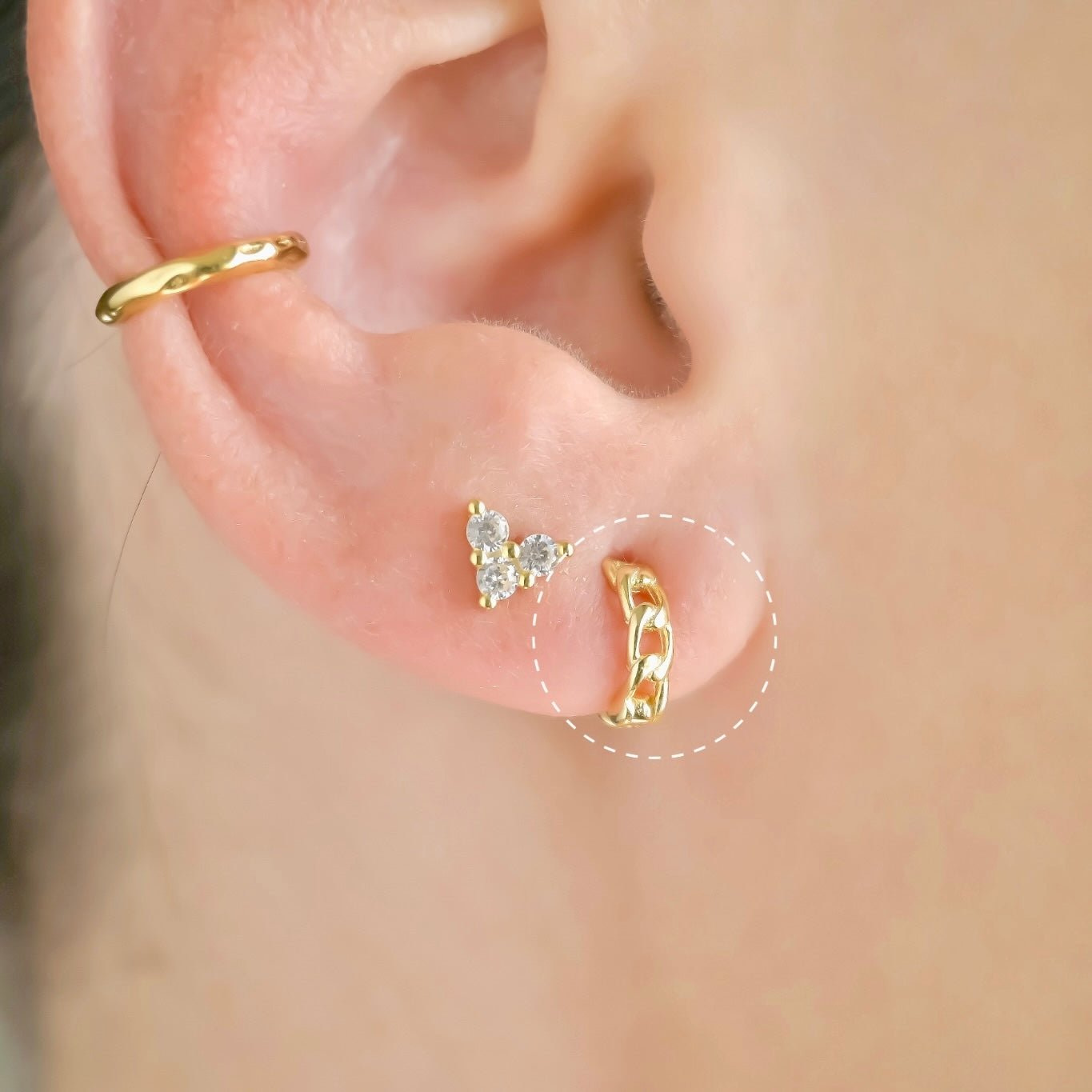 Close-up of an ear with gold earring stack with the curb link huggies highlighted with white dotted circle