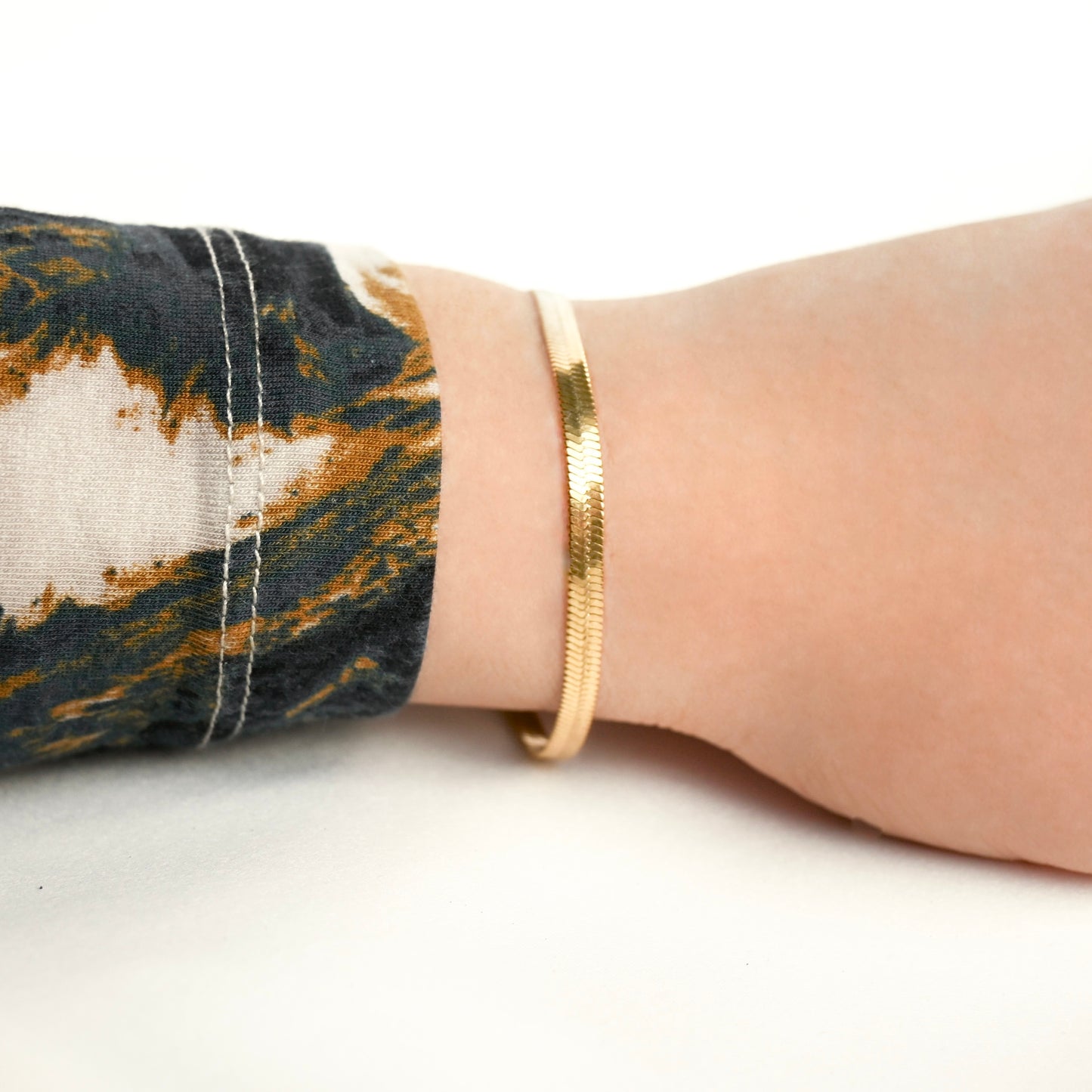 Wide gold herringbone bracelet on a wrist with a patterned sleeve against a white background