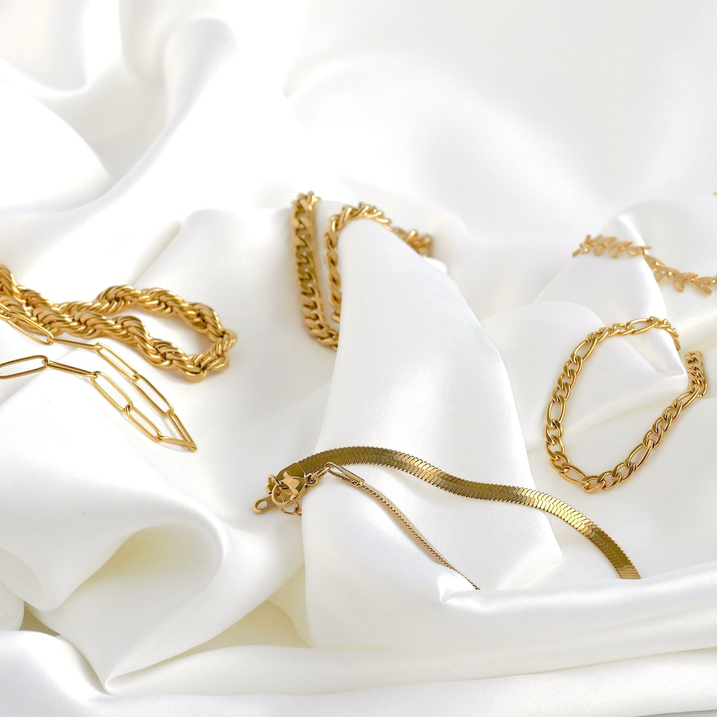 Gold chain bracelets on a white fabric background