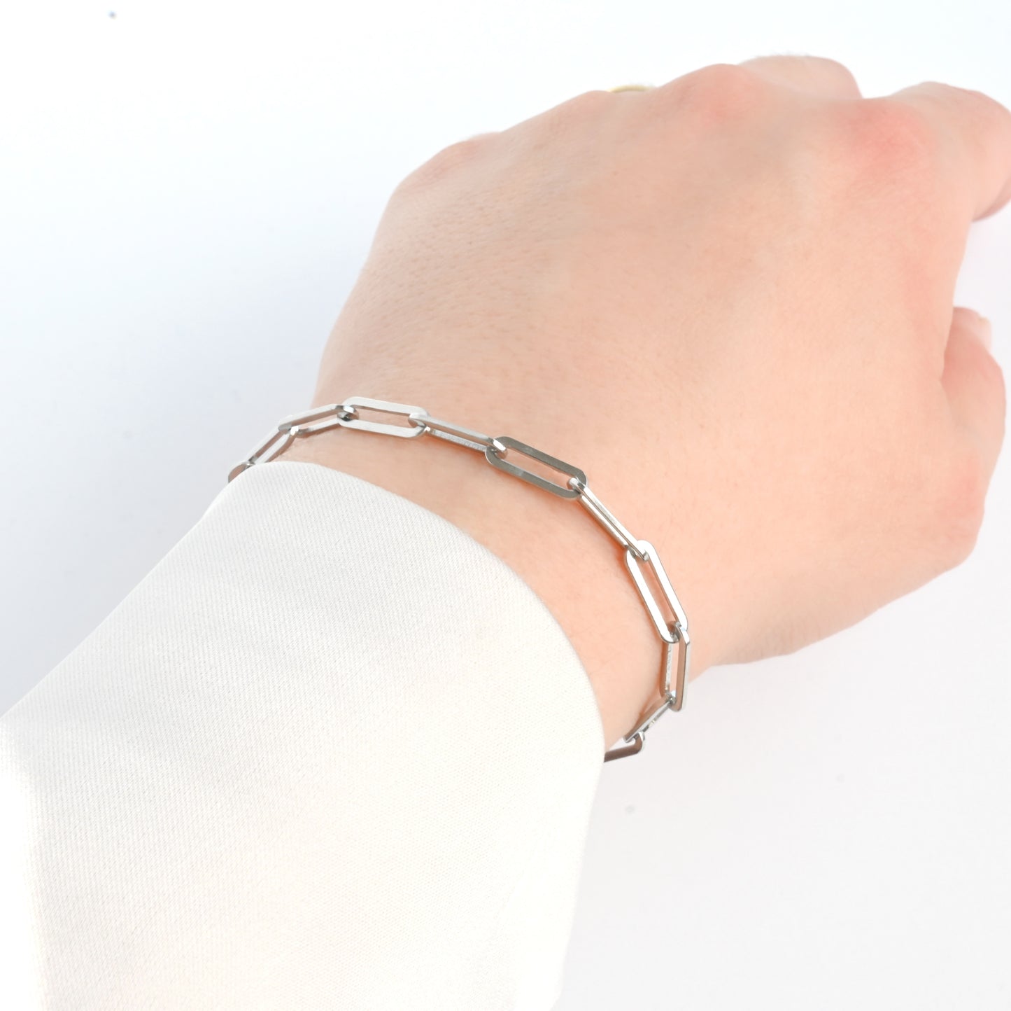 Hand wearing a thick silver paperclip chain bracelet on a white background
