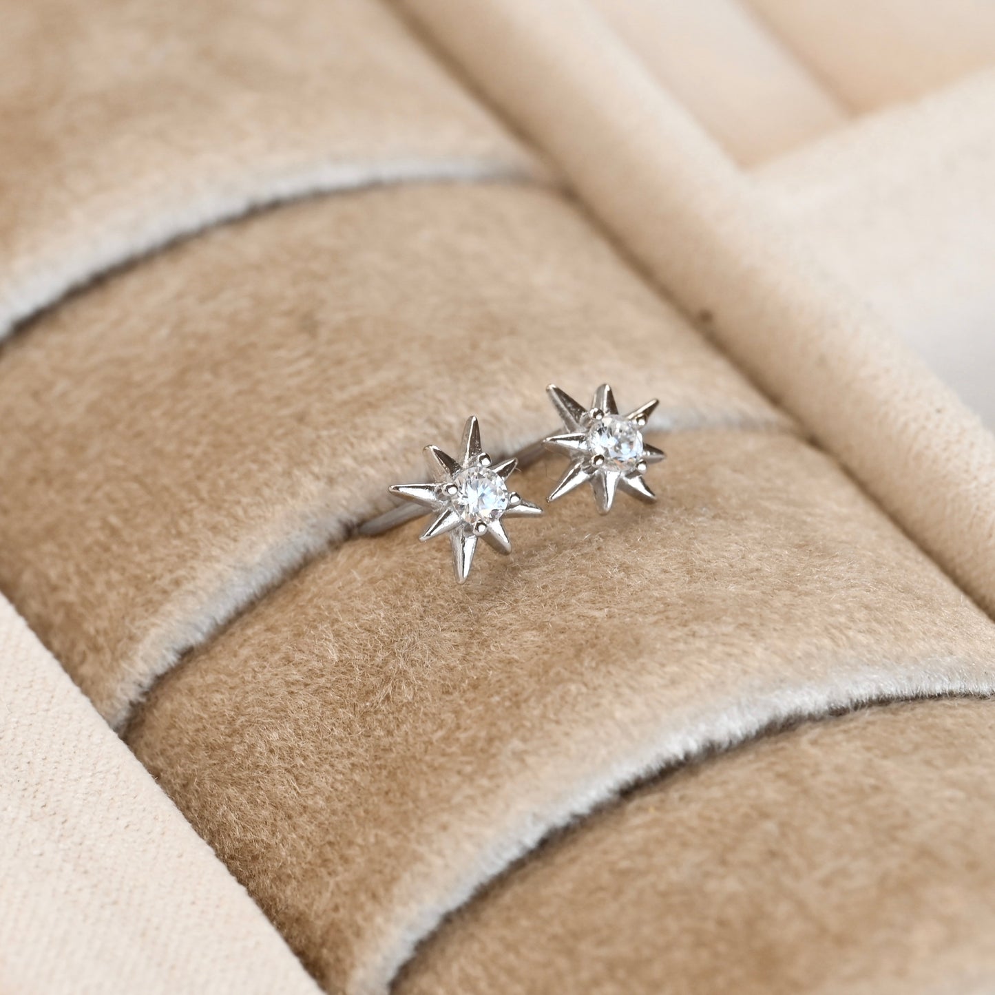Star-shaped silver earrings on a beige fabric surface