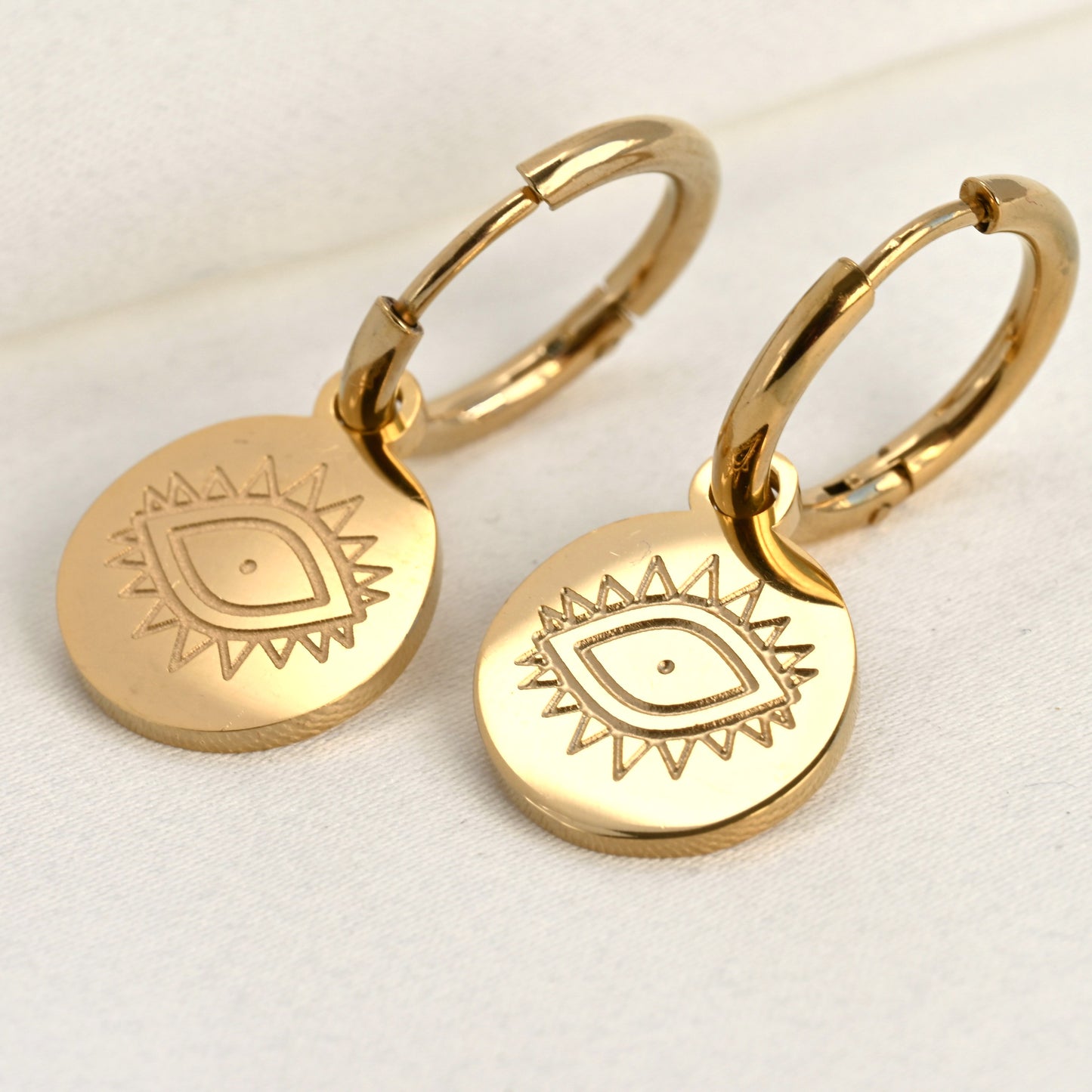 Gold hoop earrings with engraved evil eye design with lashes on a light background
