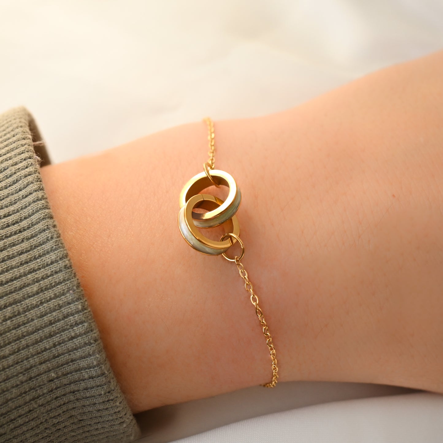 Gold shell bracelet with interlocking rings on a wrist against a neutral background