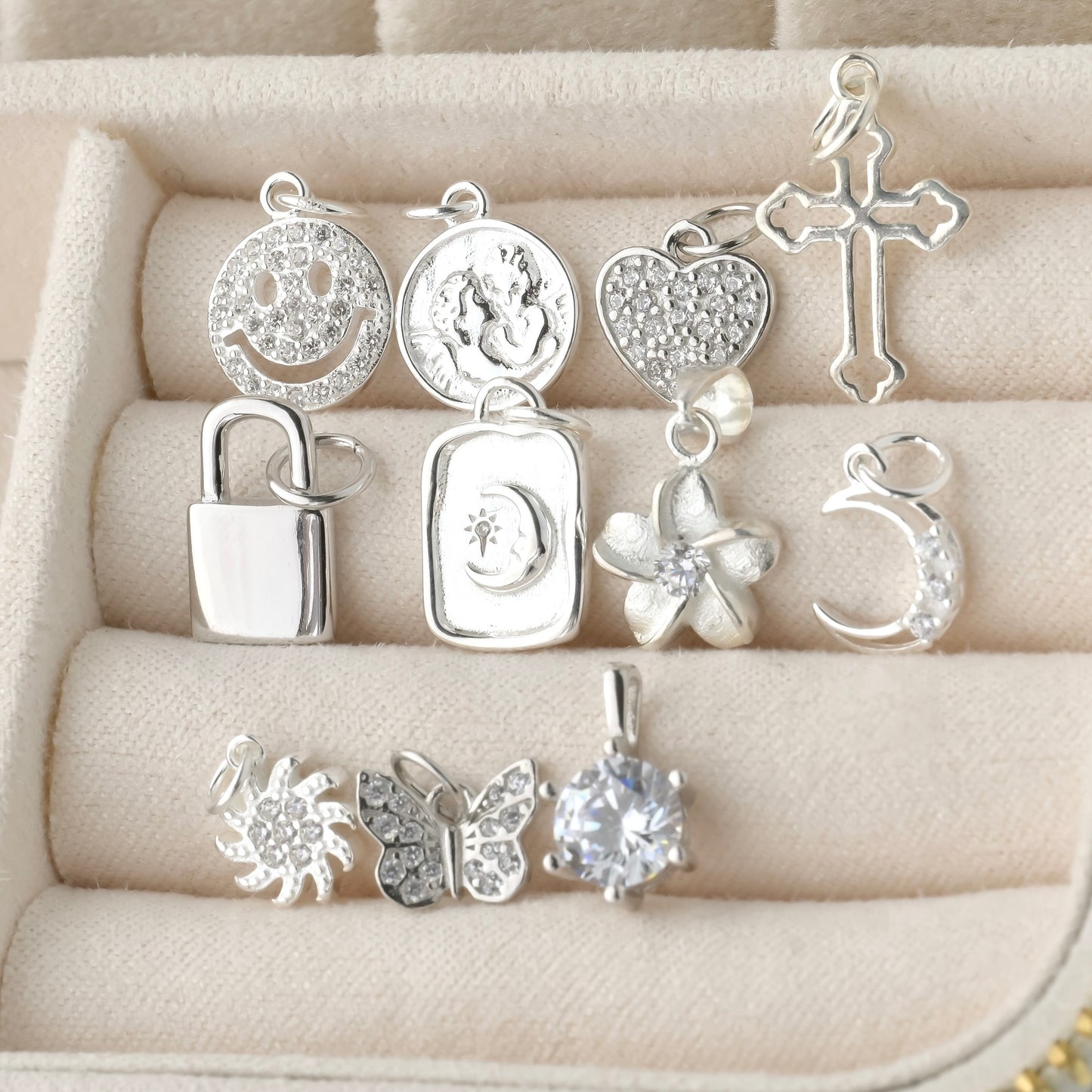 Collection of silver pendants  inlcuding smiley face, coin, heart, cross, padlock, moon, flower, sun, butterfly and solitaire on a textured beige surface