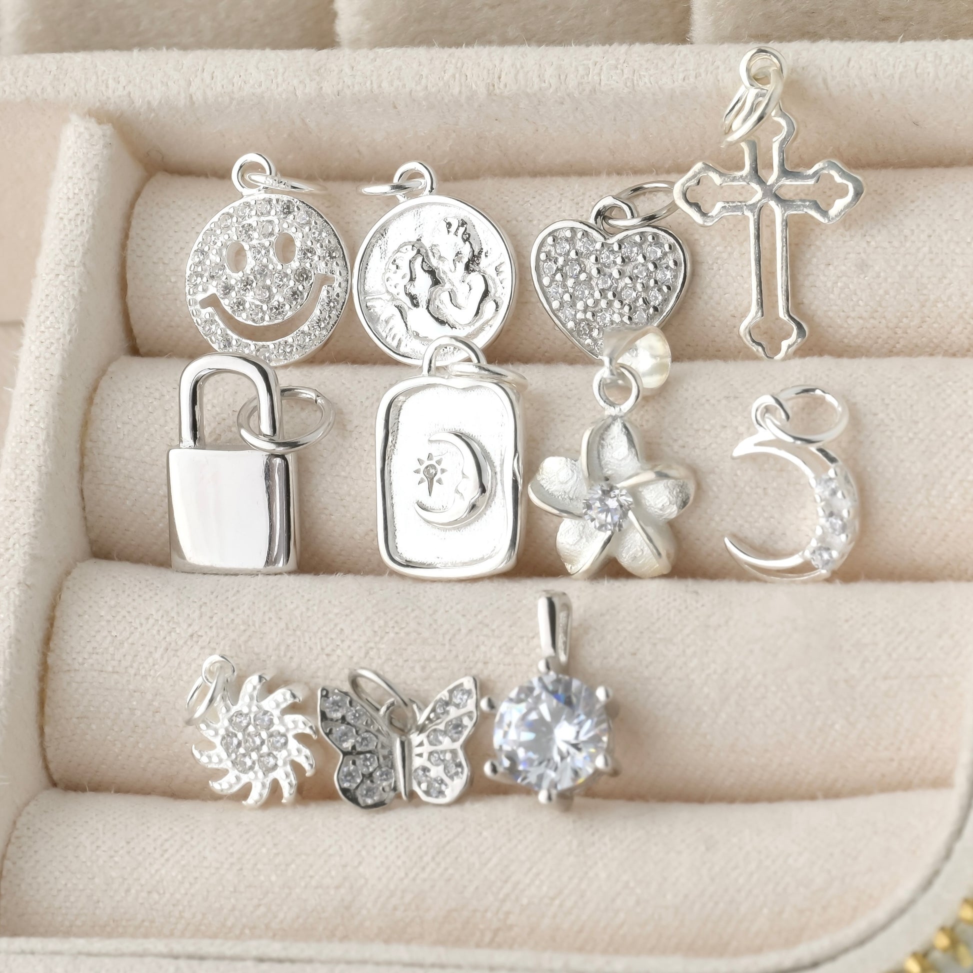 Collection of silver pendants  inlcuding smiley face, coin, heart, cross, padlock, moon, flower, sun, butterfly and solitaire on a textured beige surface