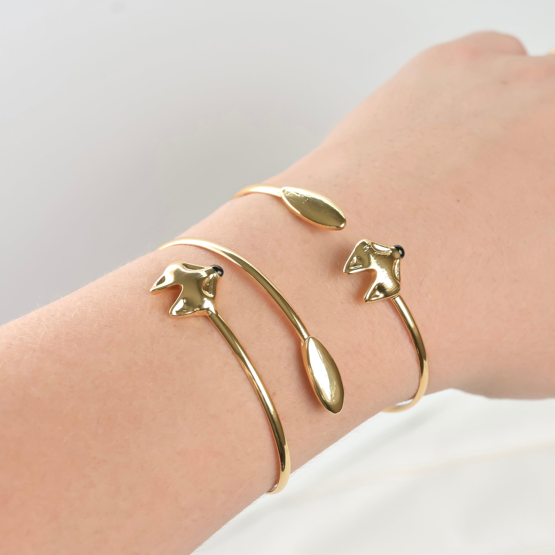 Close-up view of dainty gold fox bracelets with a  wrap cuff design on a wrist against a light background