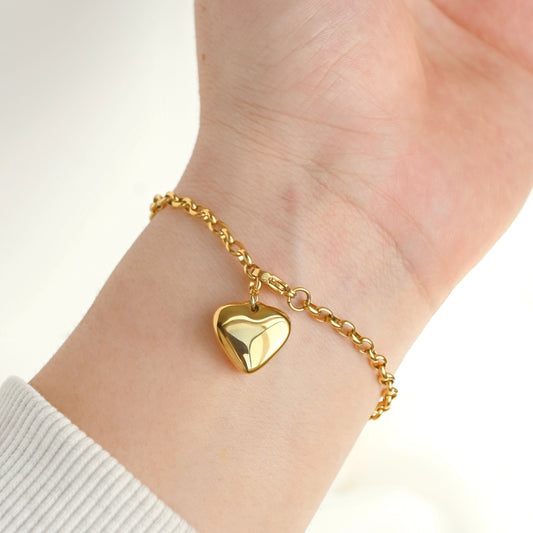 A dainty gold chain bracelet with a polished, three-dimensional heart charm, shown worn on a person's wrist.