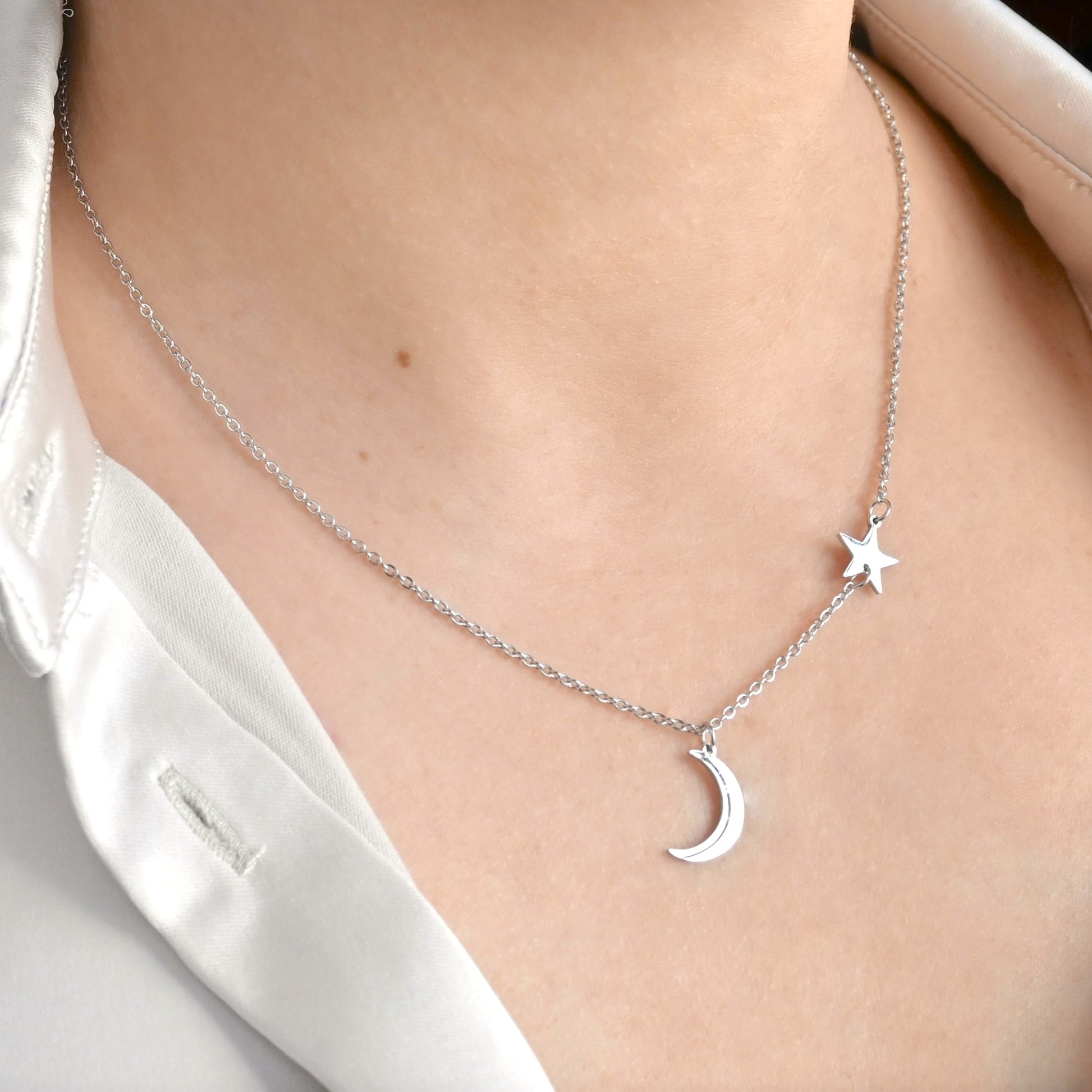 Silver necklace with moon and star pendants along a fine cable chain on a person wearing a white shirt.