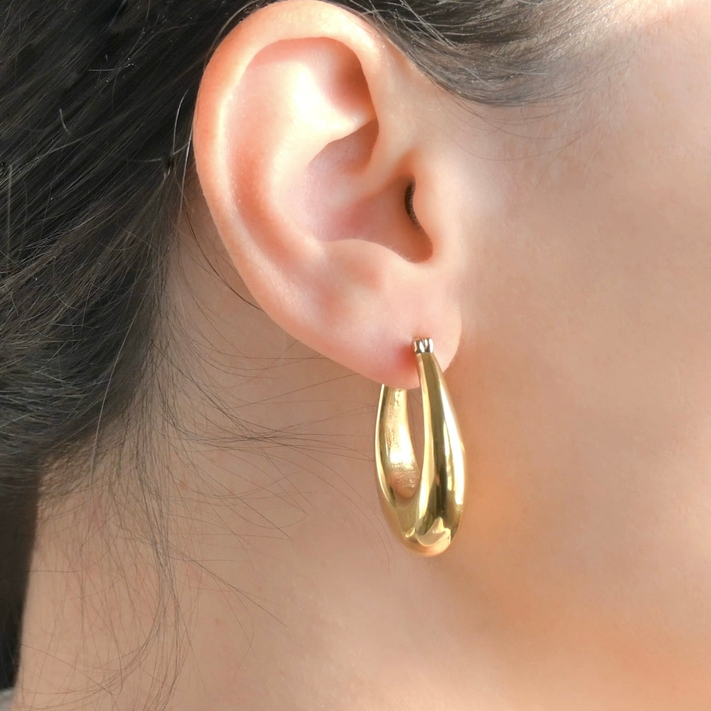Side view of a person wearing thick gold teardrop earrings