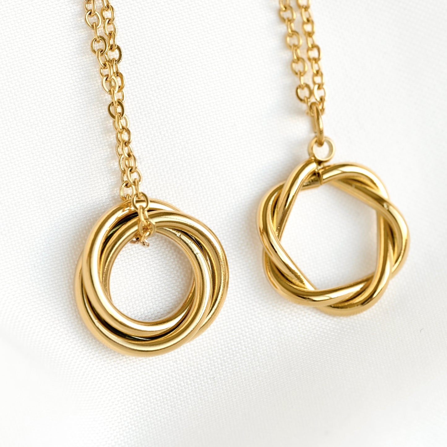 Angled close-up front view of two gold necklaces with interlocking ring pendants on a white background