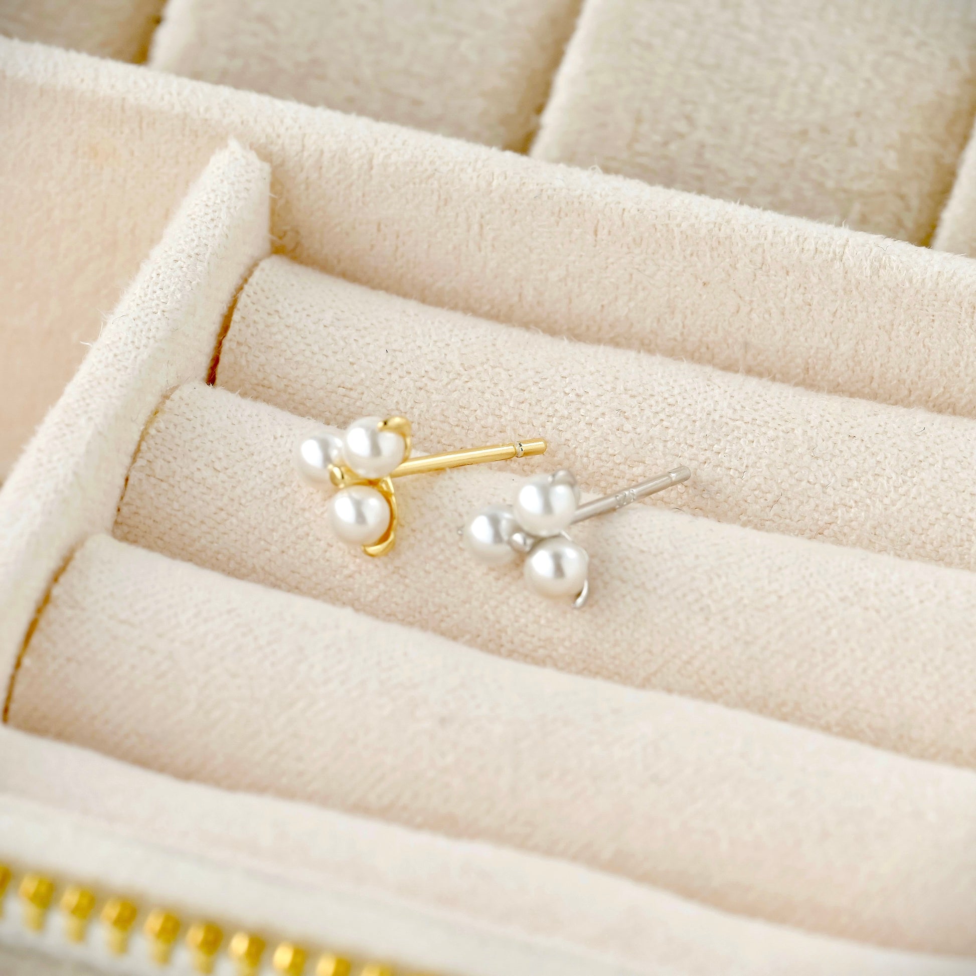 Pair of pearl stud earrings  with gold and silver posts on a beige jewelry box