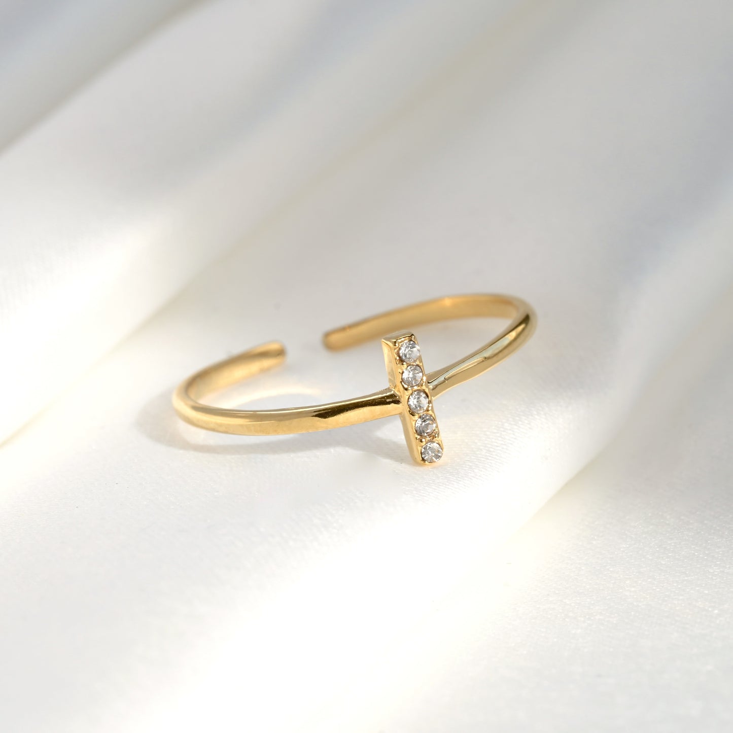 Open gold ring with a small diamond bar on a light gray background