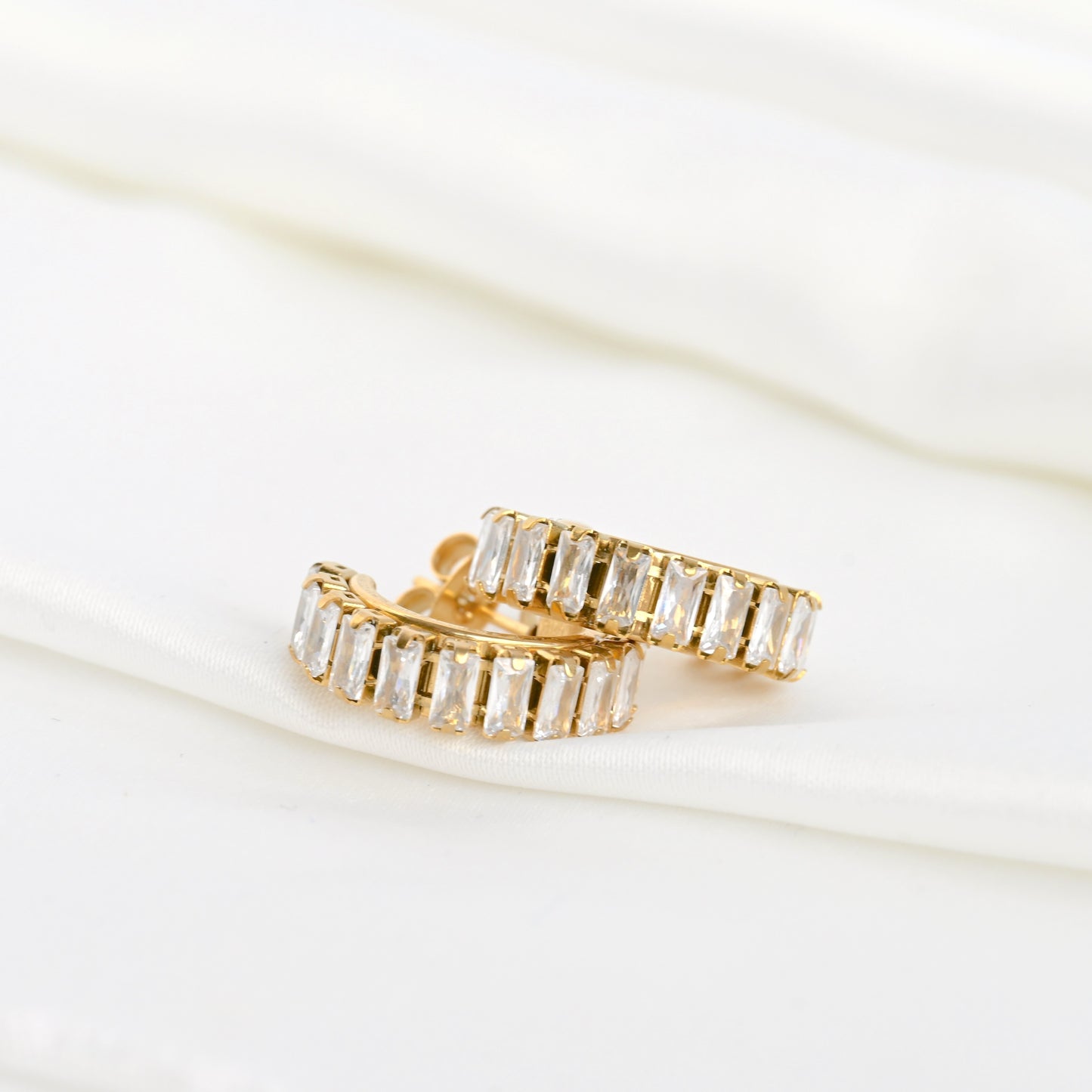 Gold baguette hoop earrings with clear gemstones stacked on a white background