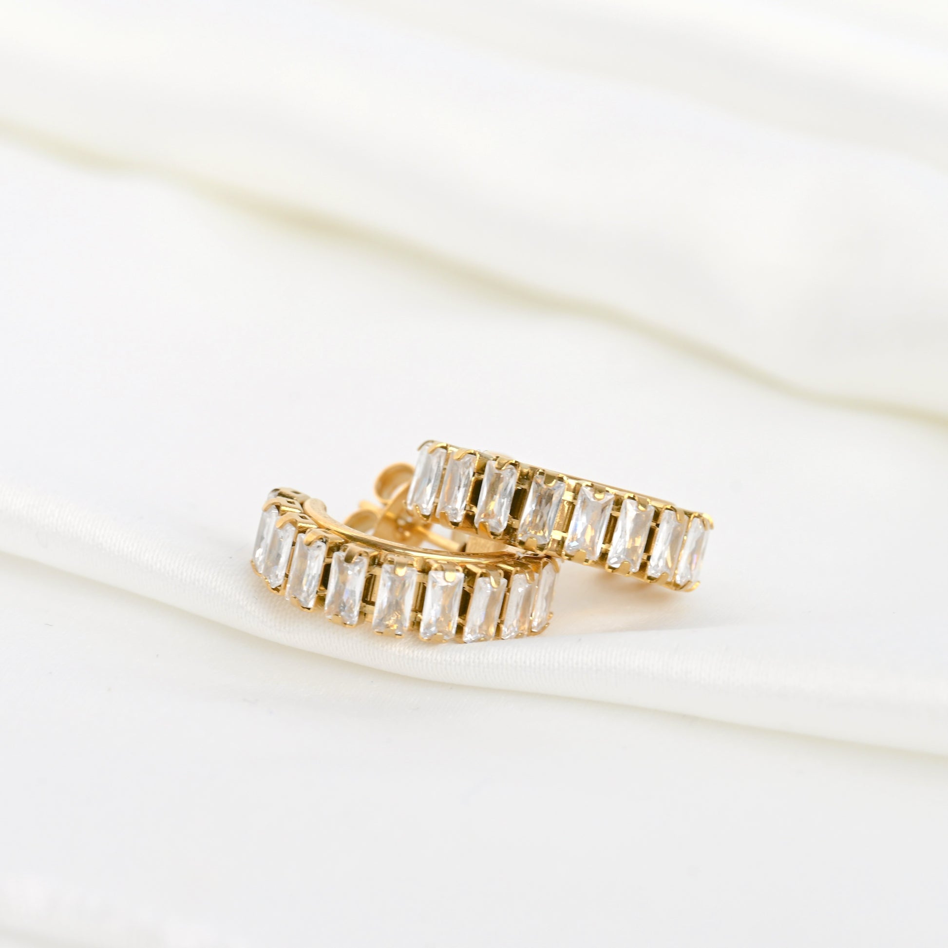 Gold baguette hoop earrings with clear gemstones stacked on a white background