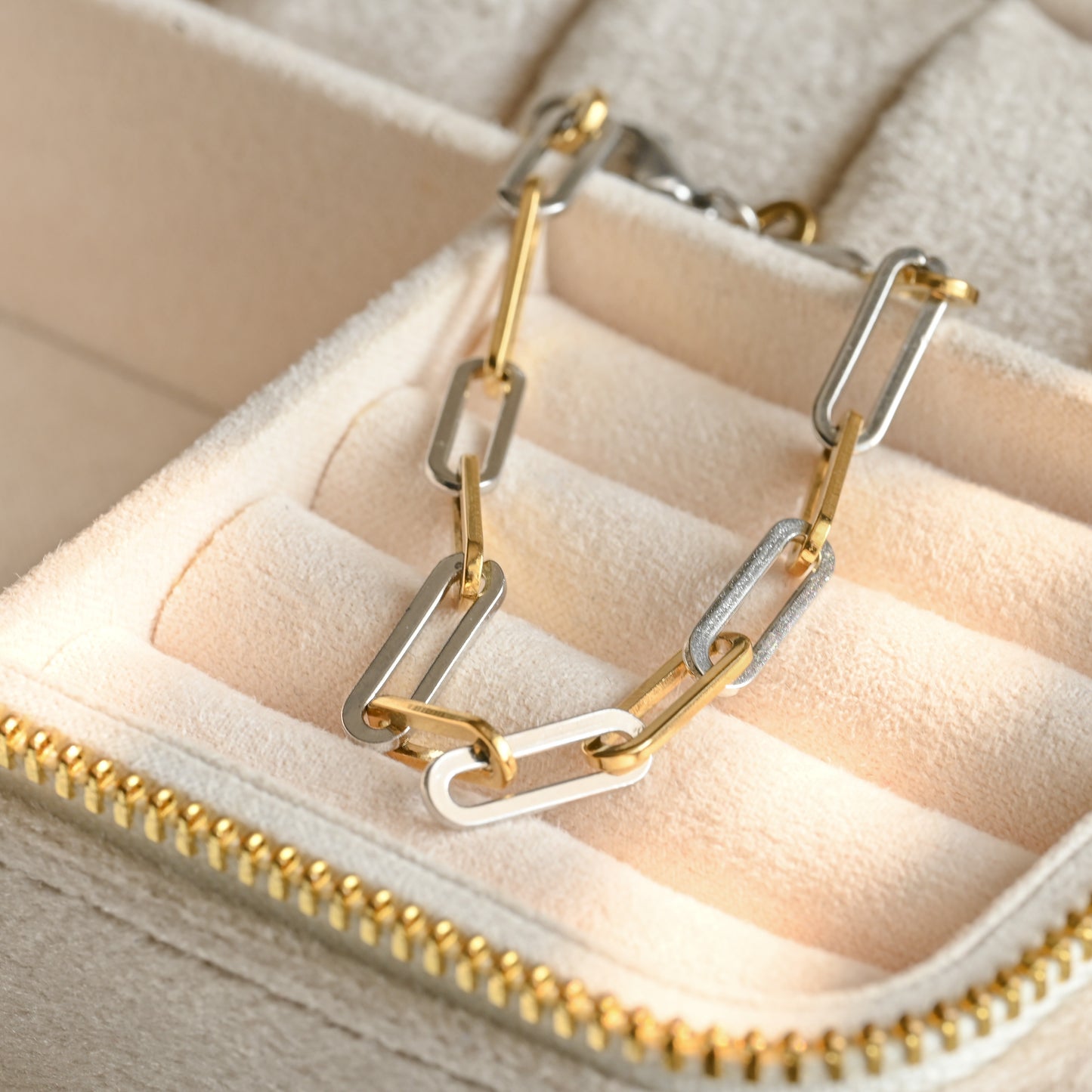 Gold and silver chain-link necklace on a beige jewelry box