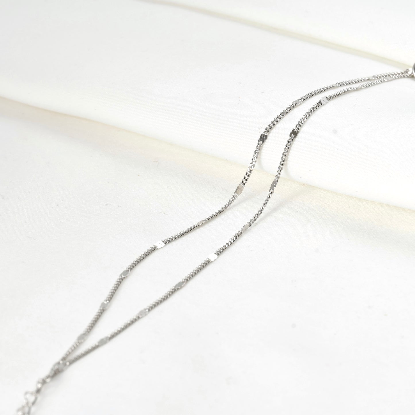 Silver chain bracelet on a white satin fabric background