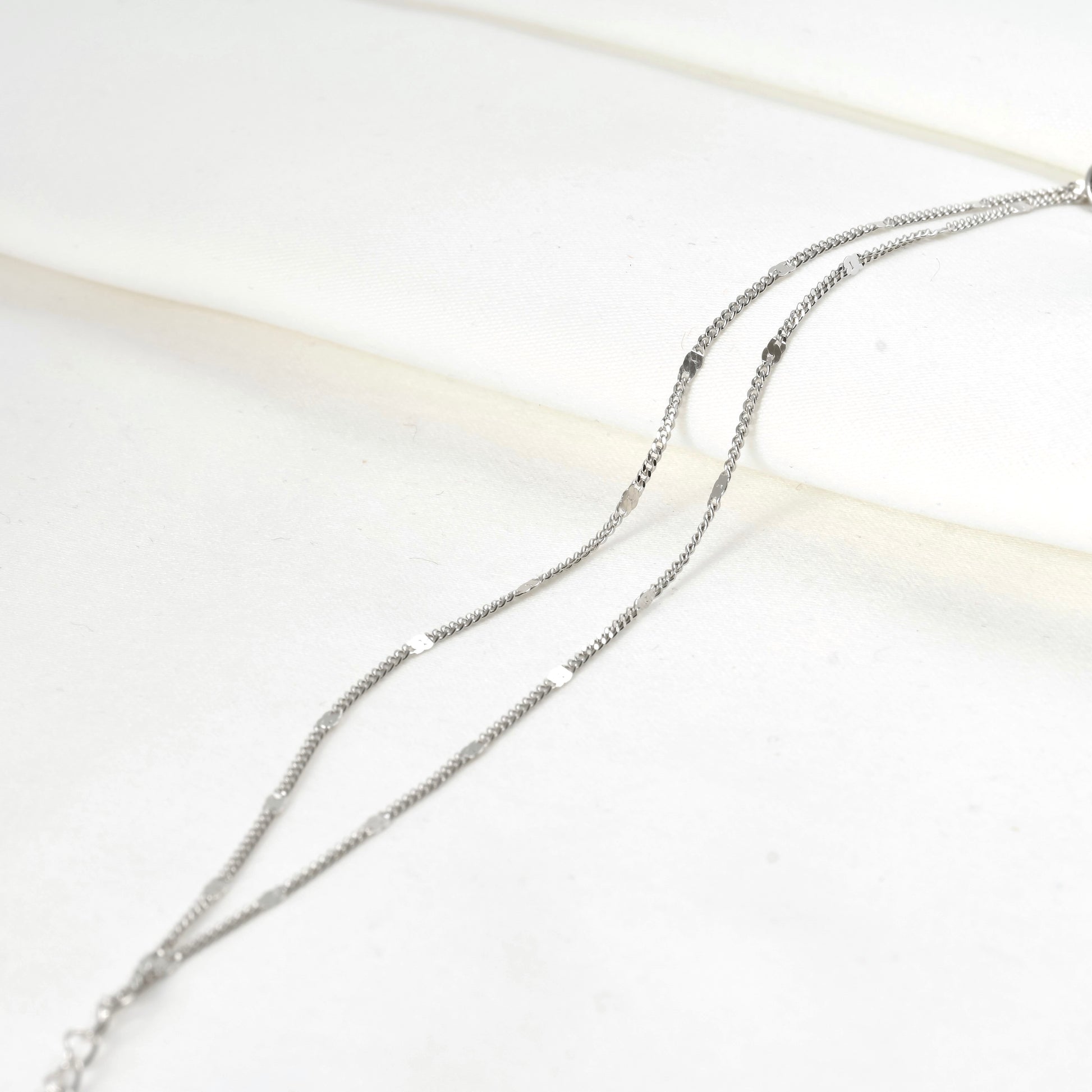 Silver chain bracelet on a white satin fabric background