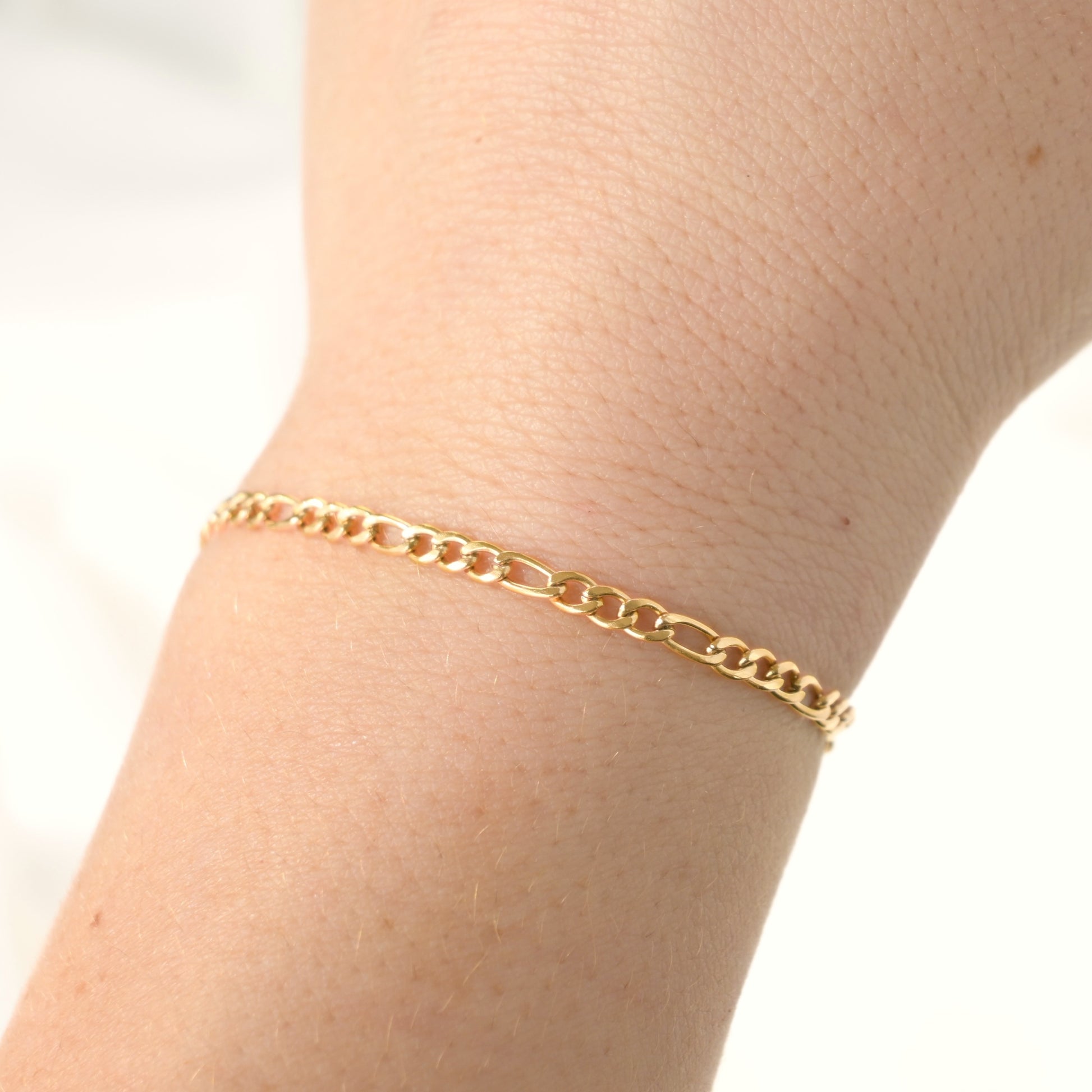 Gold figaro chain bracelet on a wrist with a plain background
