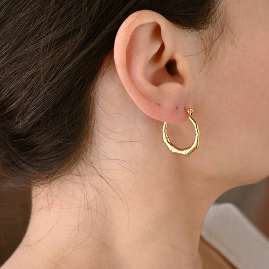 A close-up of a person's ear wearing a textured bamboo gold hoop earring.