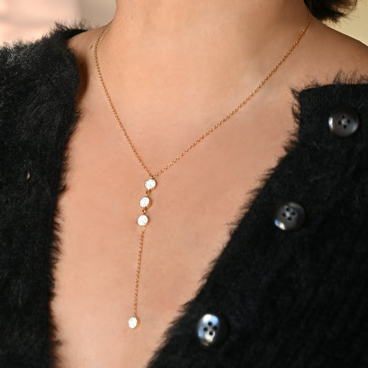 Gold Y necklace with small round pendants worn by a person in a black textured garment.