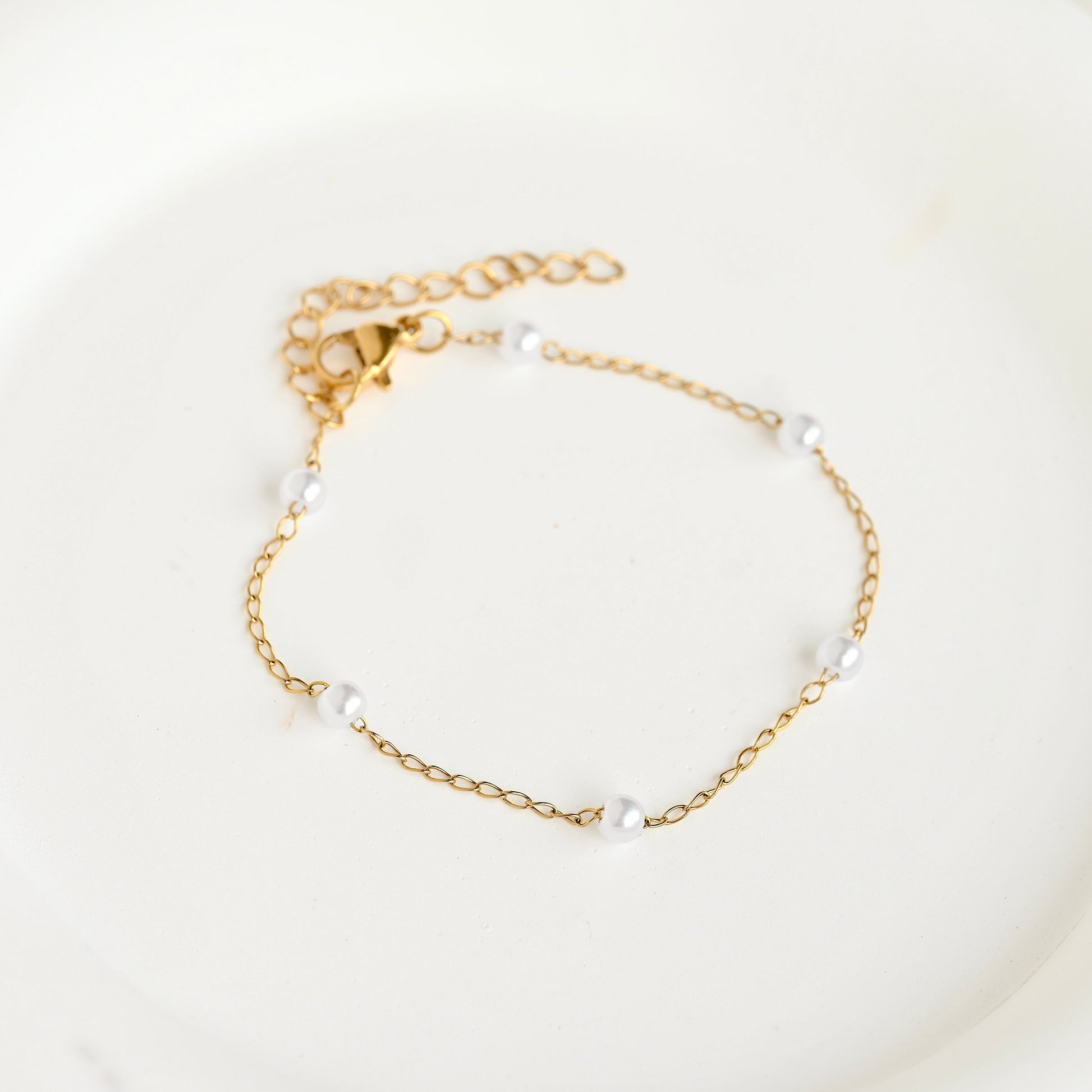 A delicate gold chain bracelet with small white pearl beads spaced along the chain, displayed on a clean white surface.