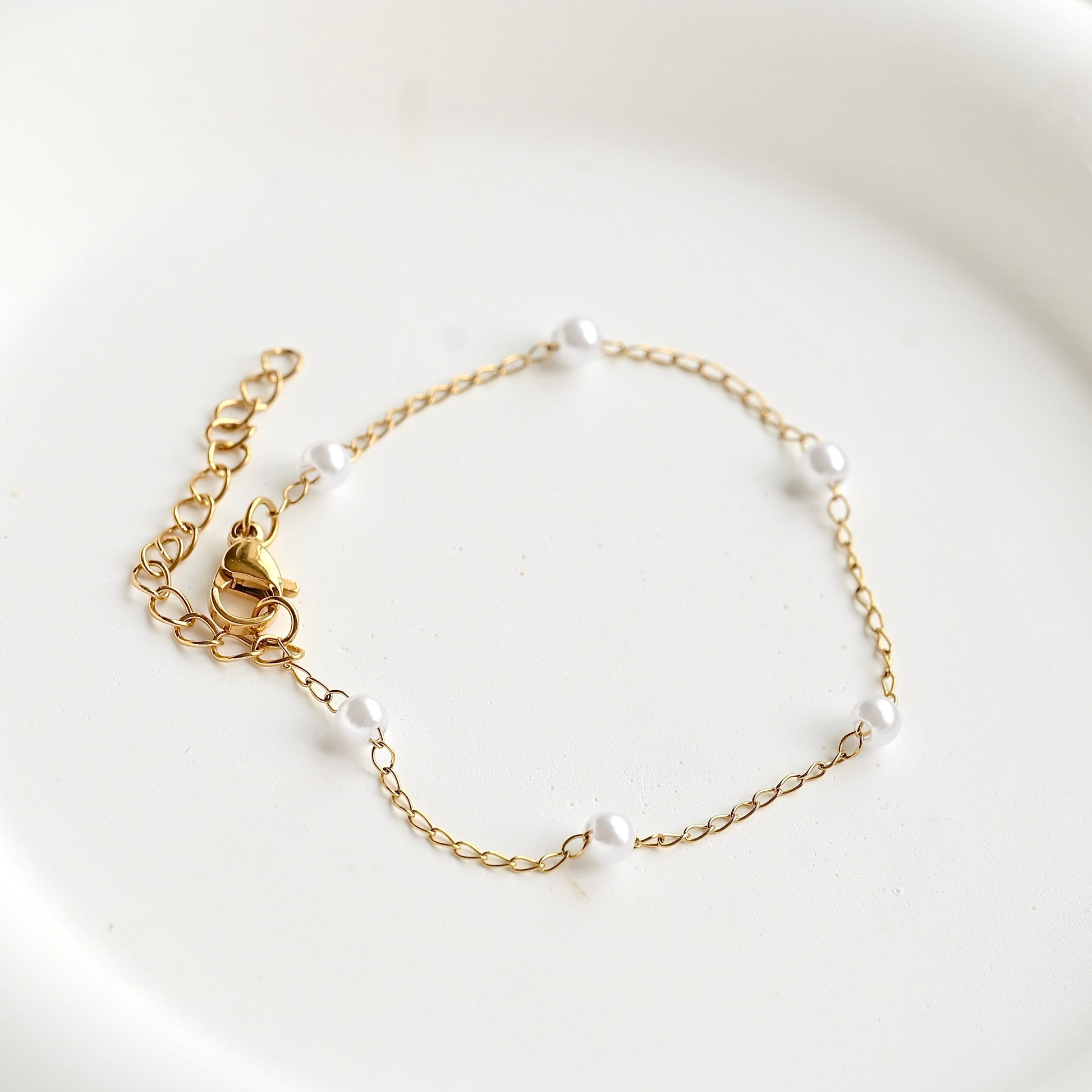 A delicate gold chain bracelet with five small white pearl beads spaced along the chain, displayed on a clean white surface.