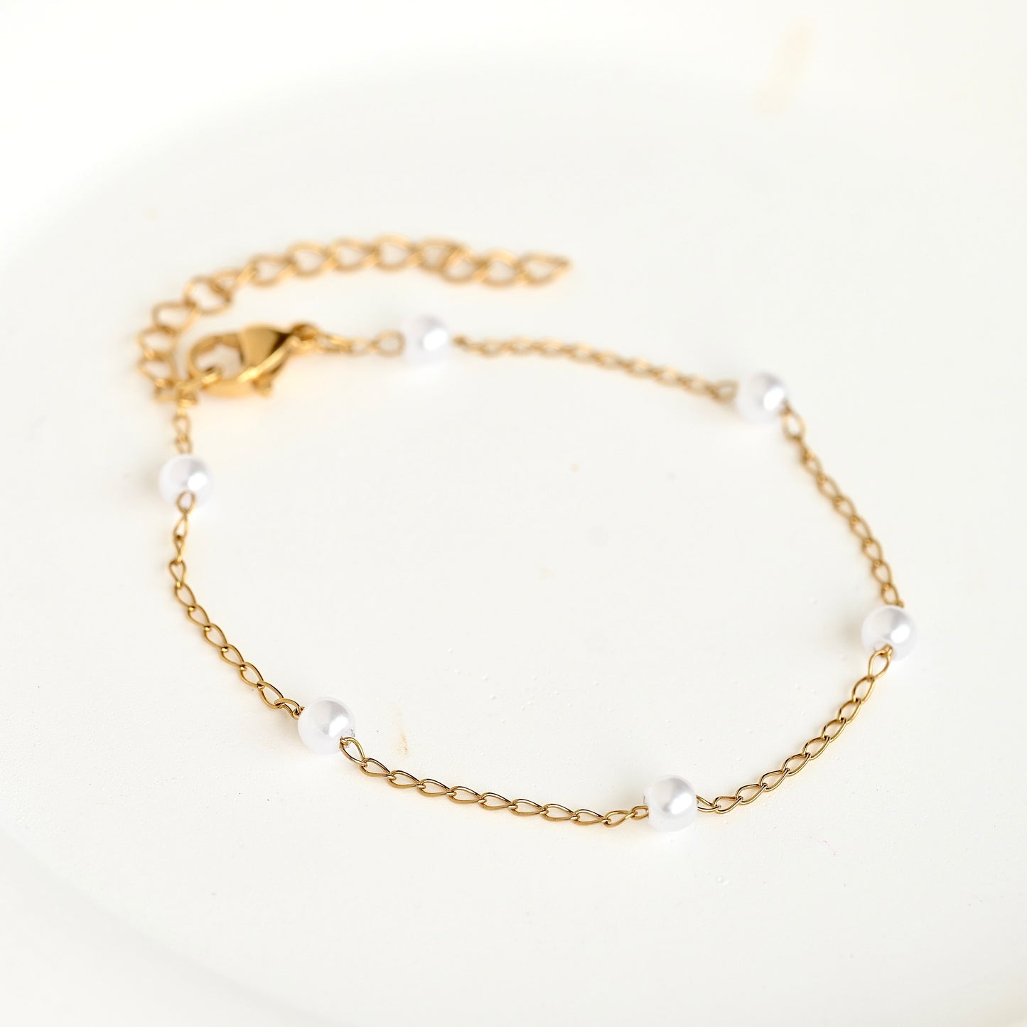 A delicate gold chain bracelet with five small white pearl beads spaced along the chain, displayed on a clean white background.