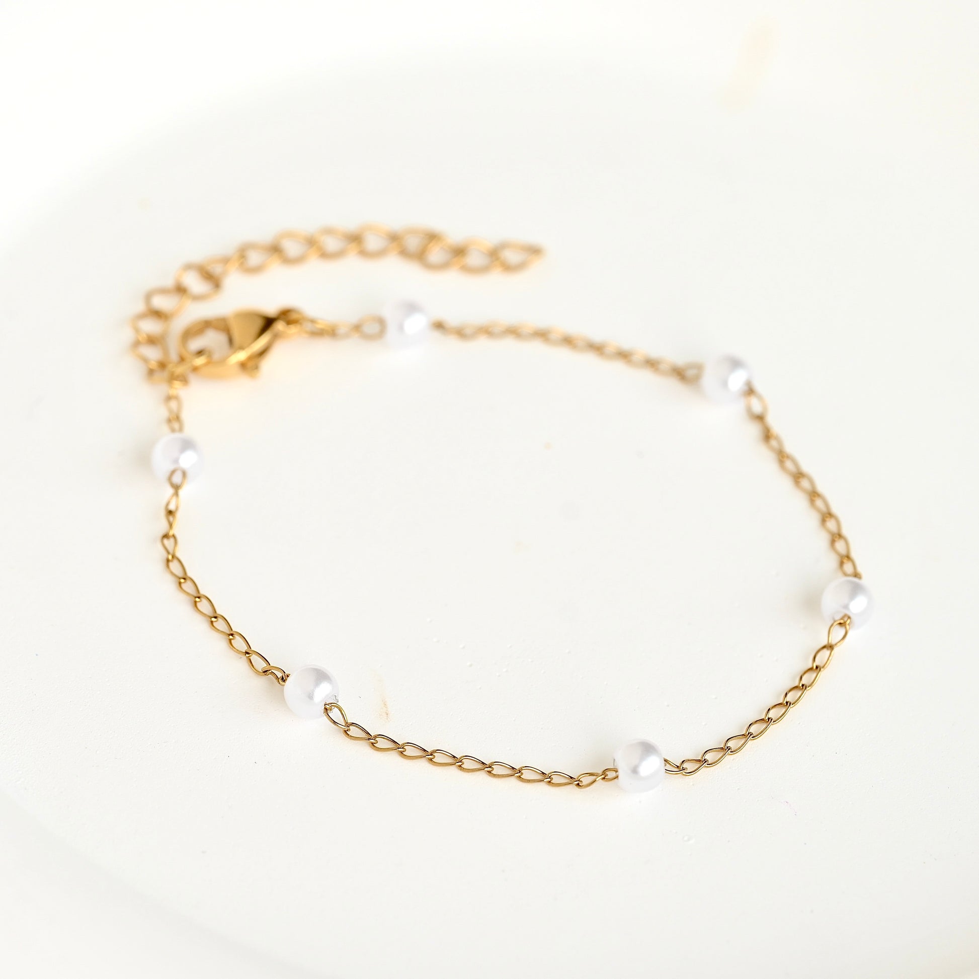 A delicate gold chain bracelet with five small white pearl beads spaced along the chain, displayed on a clean white background.
