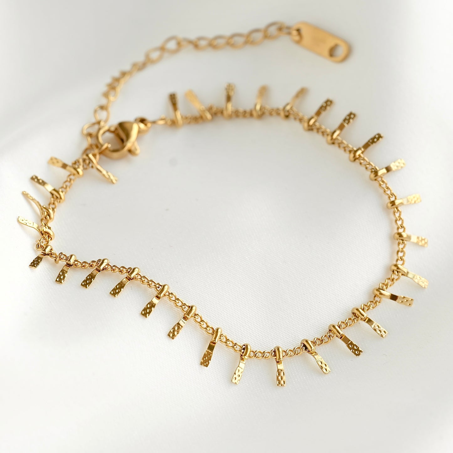 A gold chain bracelet featuring textured, spike-like dangling charms, displayed on a clean white background.