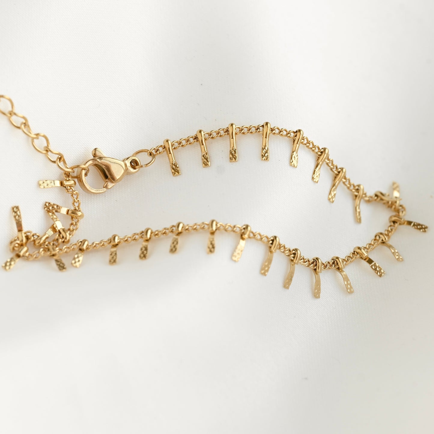 A gold chain bracelet with multiple small textured dangling spikes, displayed on a clean white background.