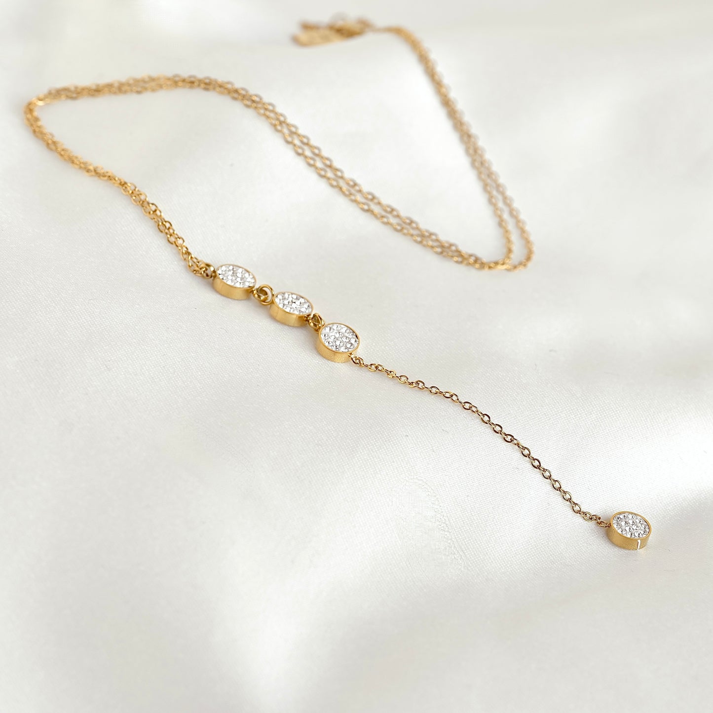 Gold Lariat necklace with small round diamond pendants on a fine cable chain, resting on white fabric