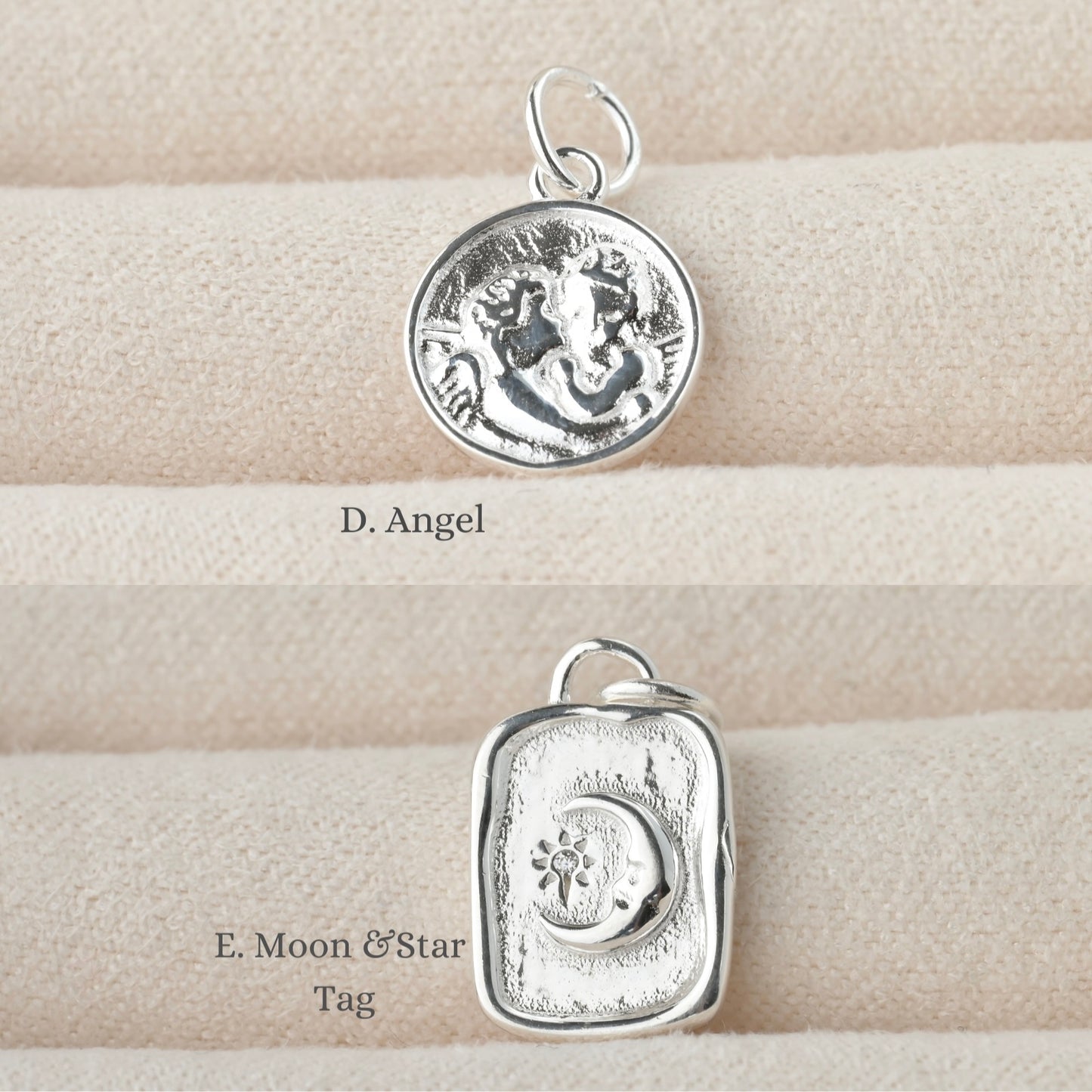 Two silver pendants on a textured beige surface,  a coin charm with two embossed angels and an organic tag charm with emmbossed moon and sun/