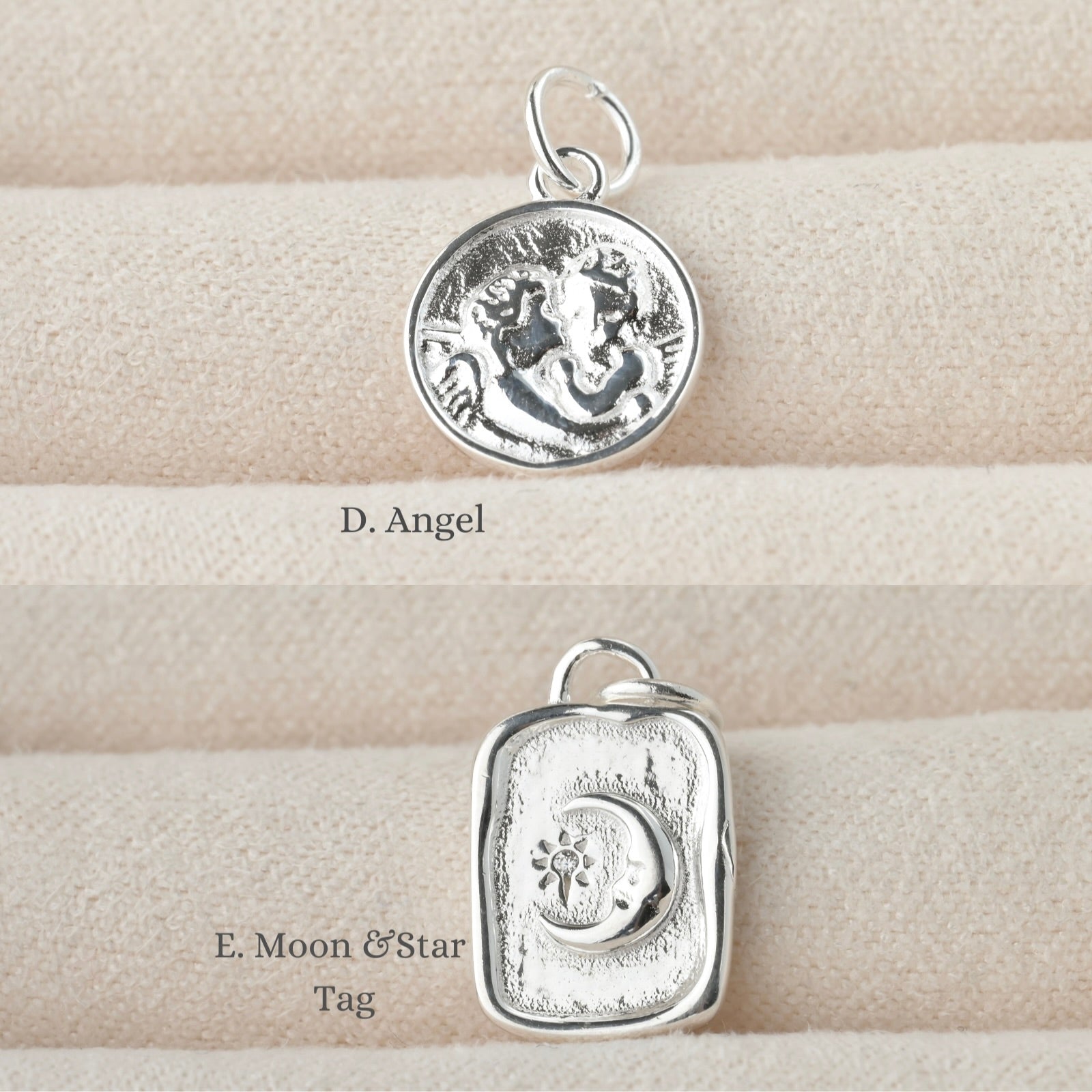 Two silver pendants on a textured beige surface,  a coin charm with two embossed angels and an organic tag charm with emmbossed moon and sun/