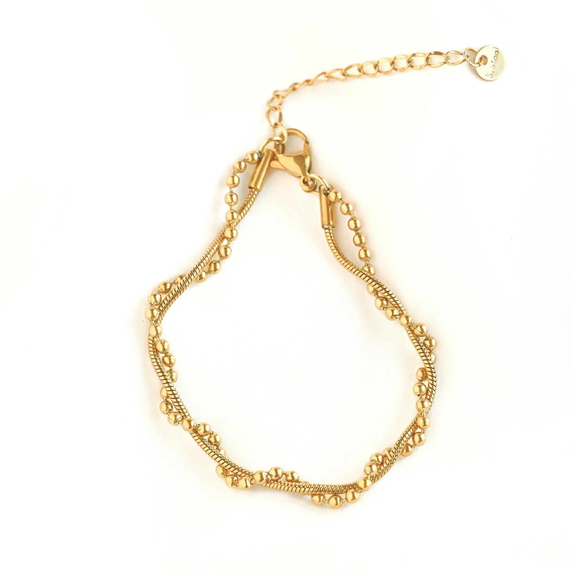 Top view of a gold-toned beaded chain bracelet with a lobster clasp and an adjustable extender chain featuring a small round tag, displayed on a clean white background.