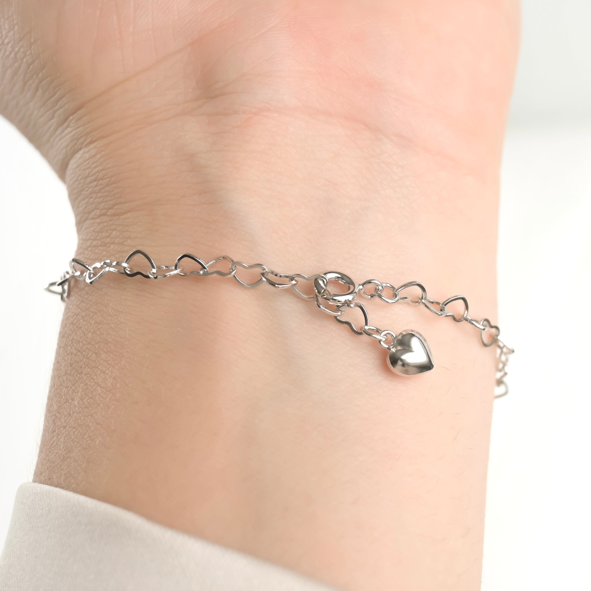 Silver heart link chain bracelet with a puffy heart charm  on the end on a wrist against a white background
