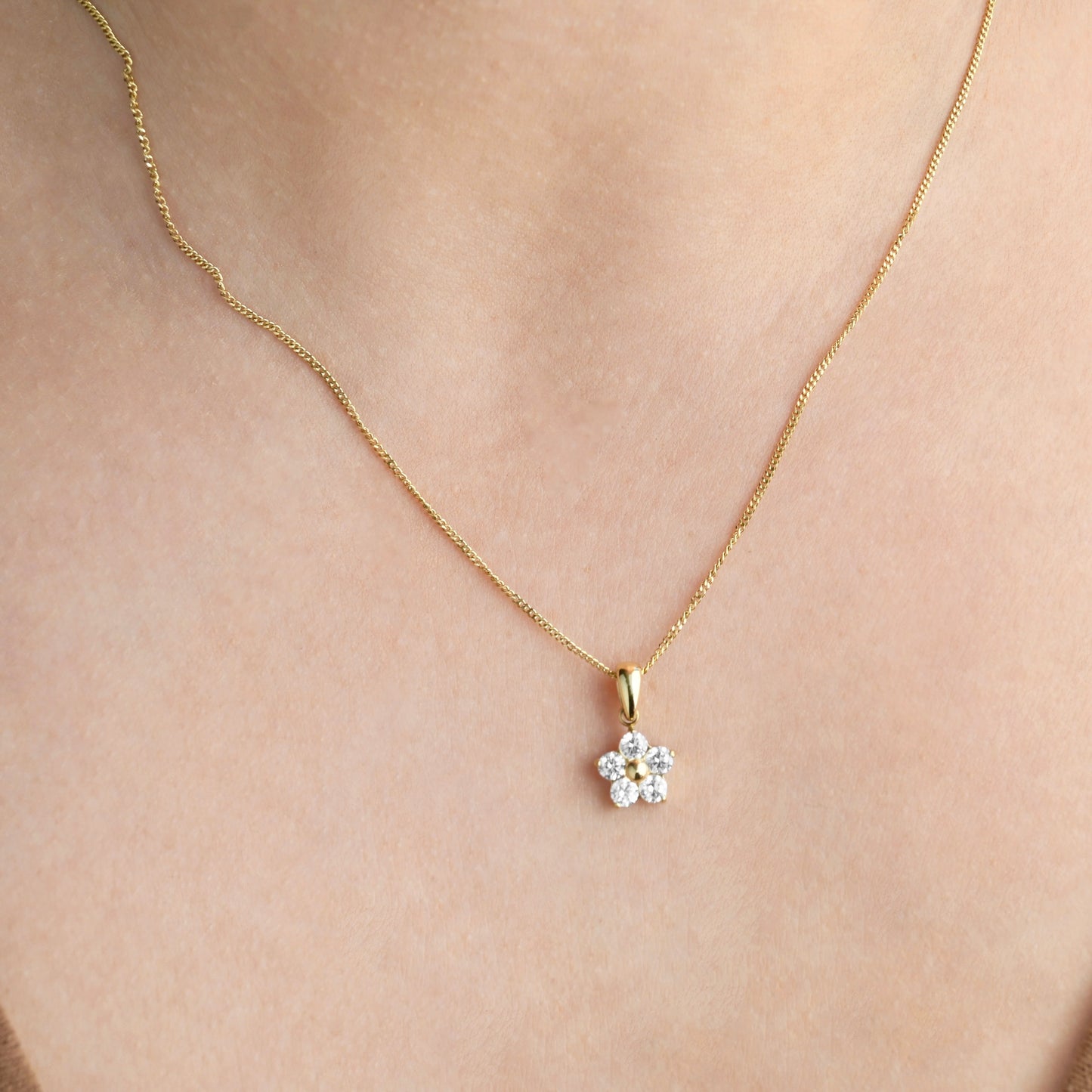 Gold necklace with a small diamond floral pendant on a person's neck