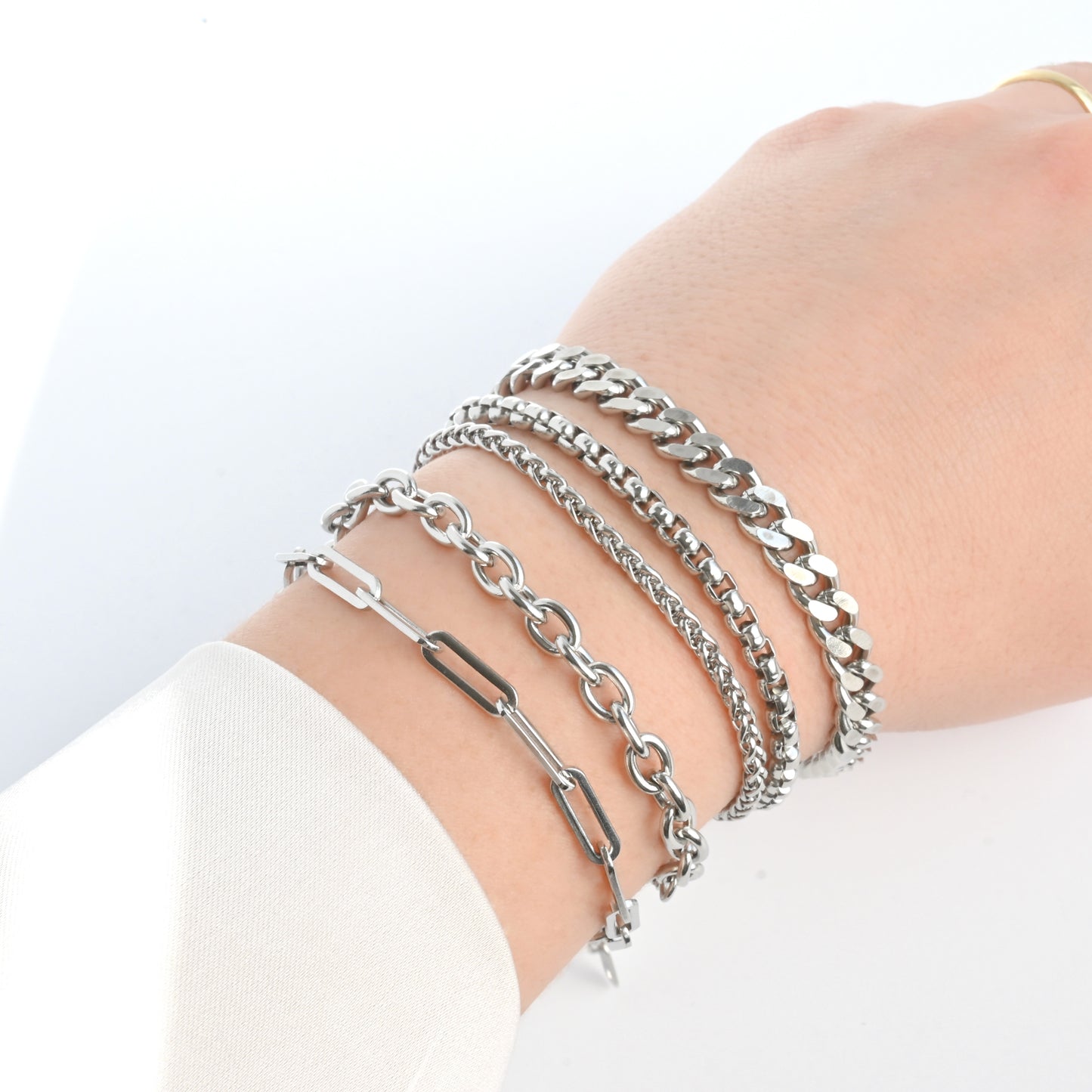 Stack of thick silver chain bracelets on a wrist against a white background